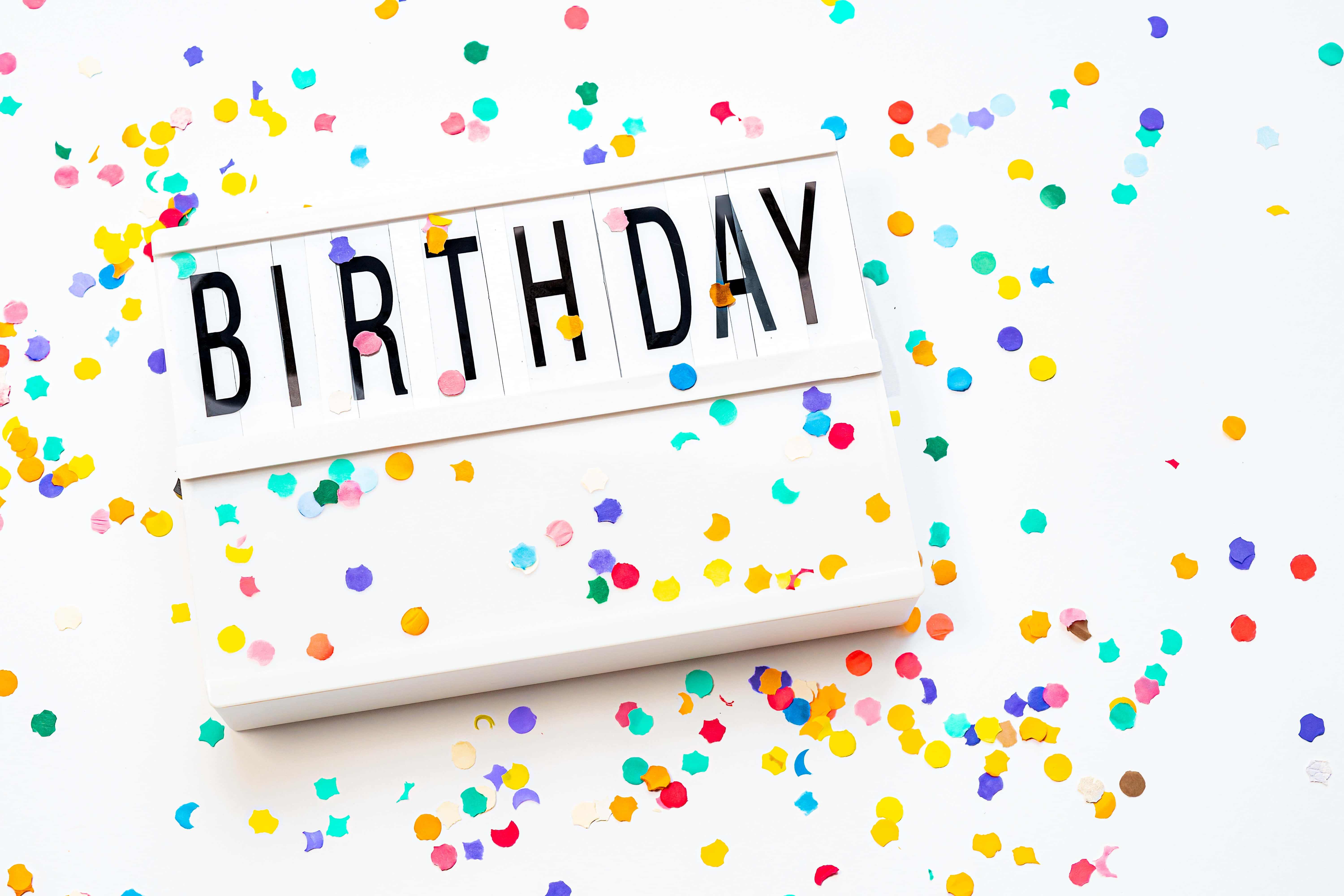 High Resolution Happy Birthday 桌布 壁紙 — 一個白色燈箱，以粗體黑色字母顯示「BIRTHDAY」，周圍有彩色紙屑散落在明亮的白色表面上。