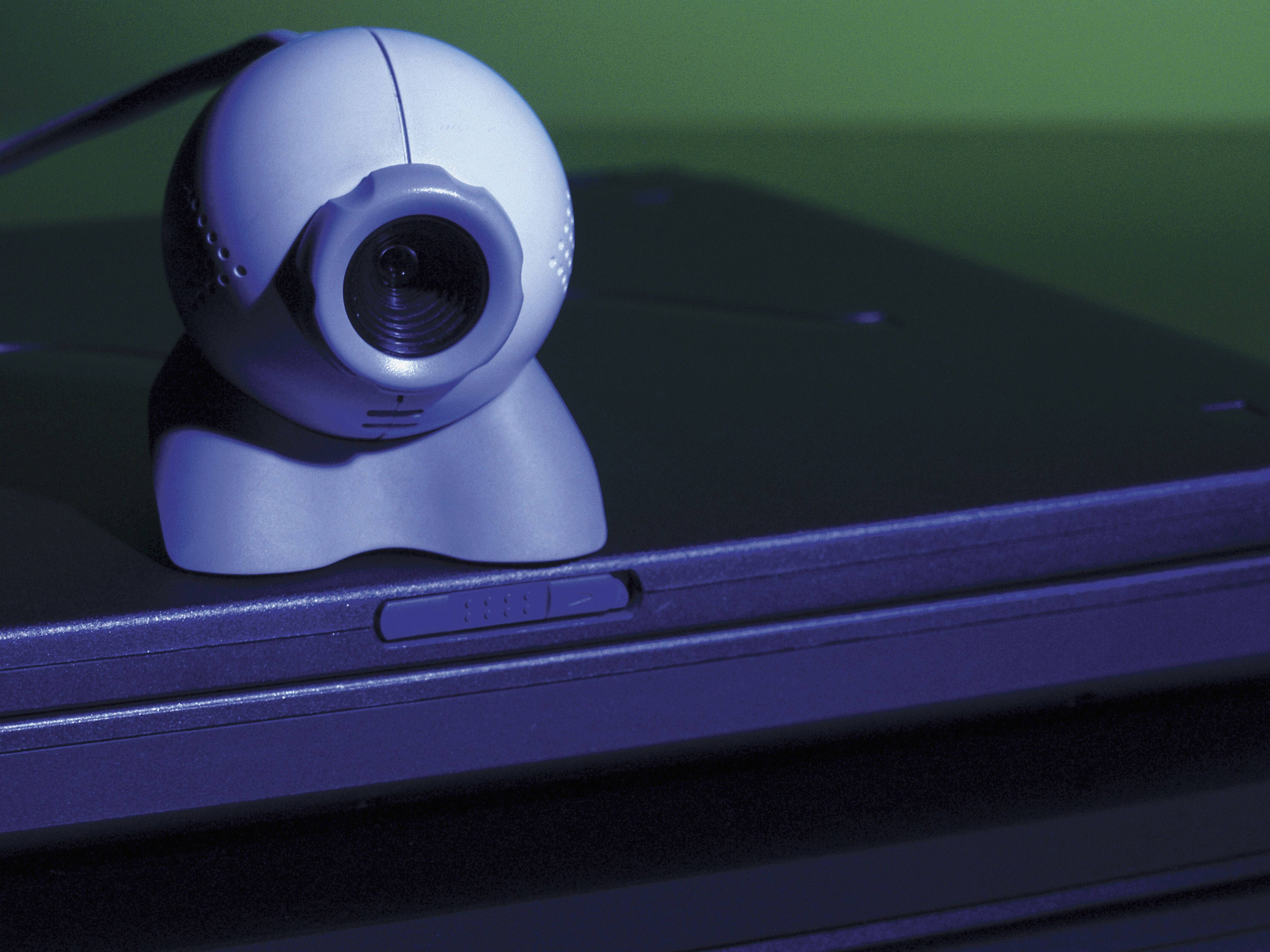 Webcam 桌布 壁紙 — 一個白色球形網路攝影機放在筆記型電腦上，在冷色調的藍色和綠色燈光下投射出柔和陰影。