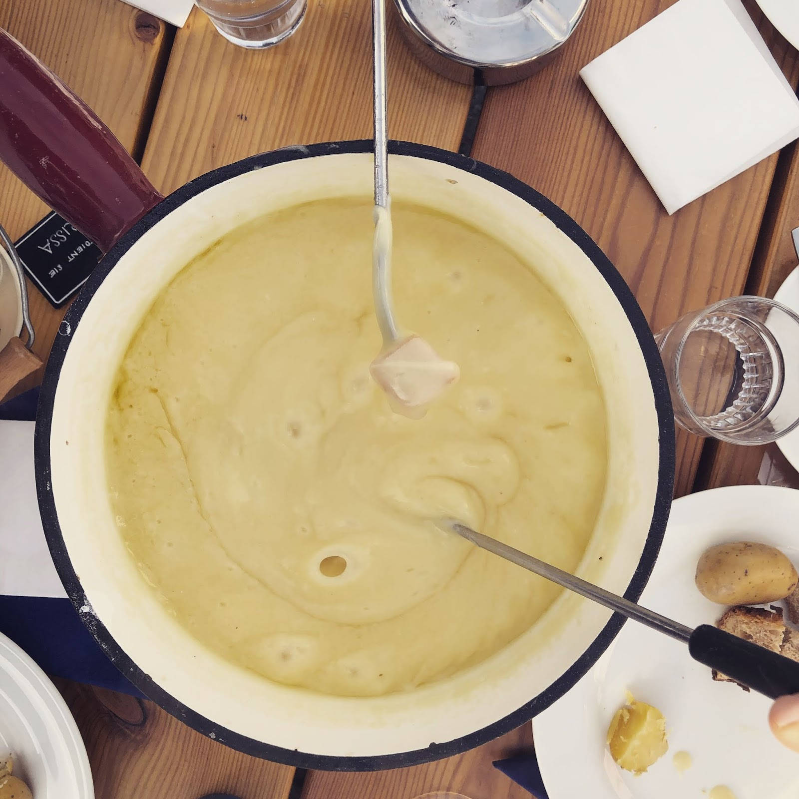 Cheese 桌布 壁紙 — 一個白色琺瑯鍋中冒泡的奶油起司火鍋，叉子蘸著麵包和馬鈴薯放在木桌上。