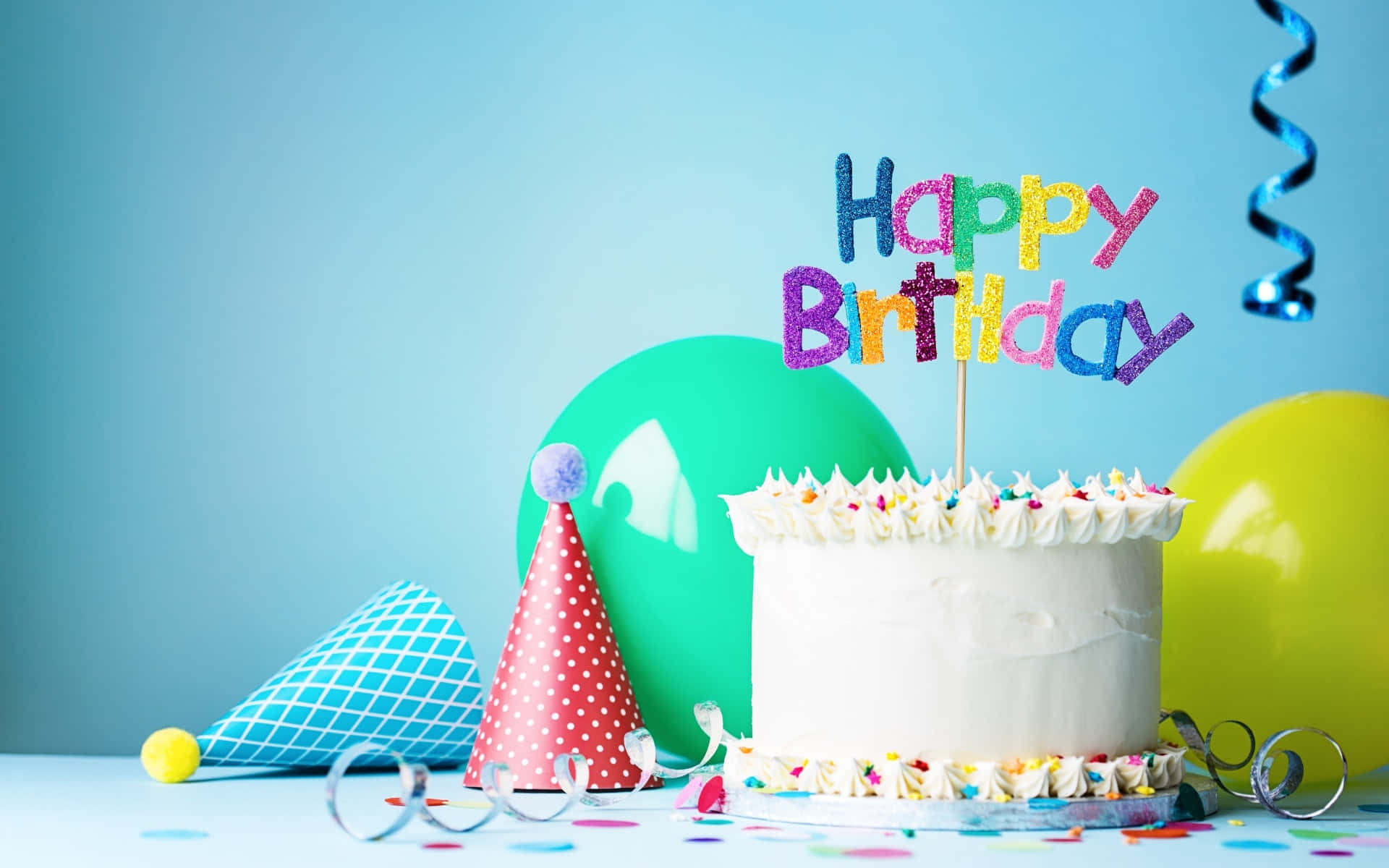 Confetti 桌布 壁紙 — 一個白色生日蛋糕，上面有彩色糖粒和閃亮的「Happy Birthday」裝飾，周圍環繞著派對帽和氣球。