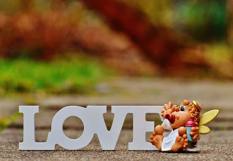 愛心 桌布 壁紙 — 一個白色的「LOVE」標誌放在人行道上，旁邊有一個拿著瓶子的小天使公仔。