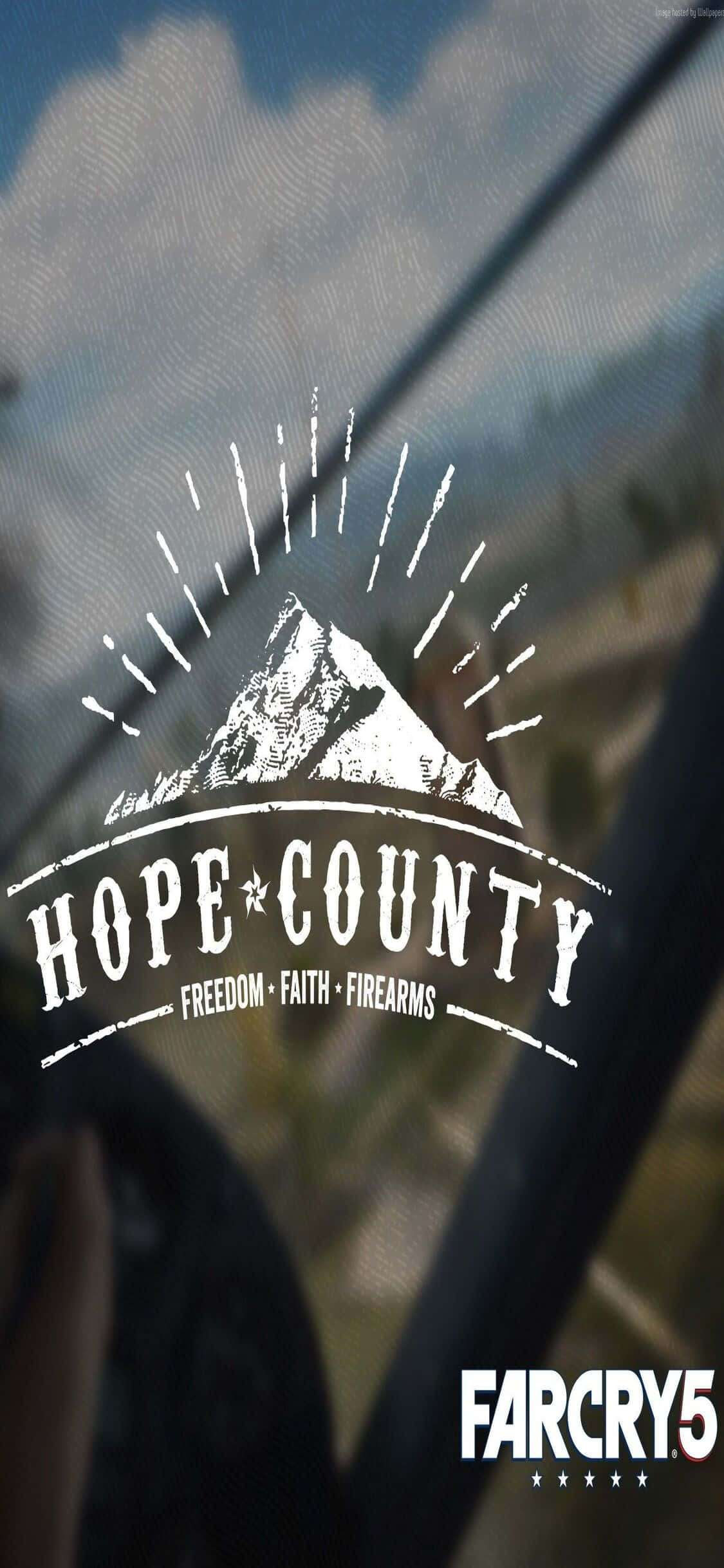 iPhone Xs Far Cry 5 桌布 壁紙 — 一個白色的Hope County標誌，帶有山脈和太陽爆發圖形，疊加在透過車窗看到的模糊景色上。