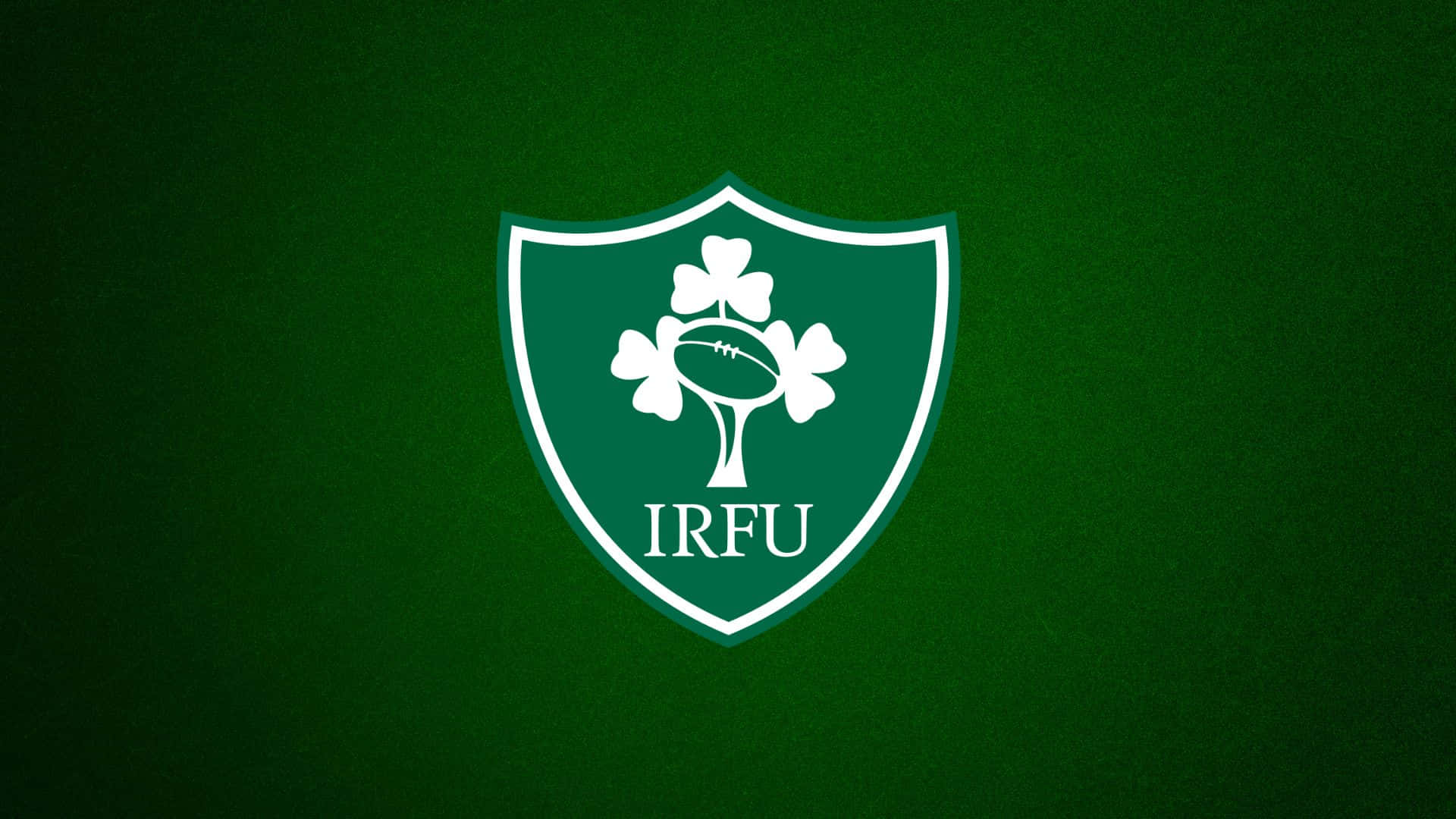 Ireland Rugby 桌布 壁紙 — 一個白色的愛爾蘭橄欖球聯盟徽章，中央有酢漿草和橄欖球，置於有紋理的深綠色背景上。