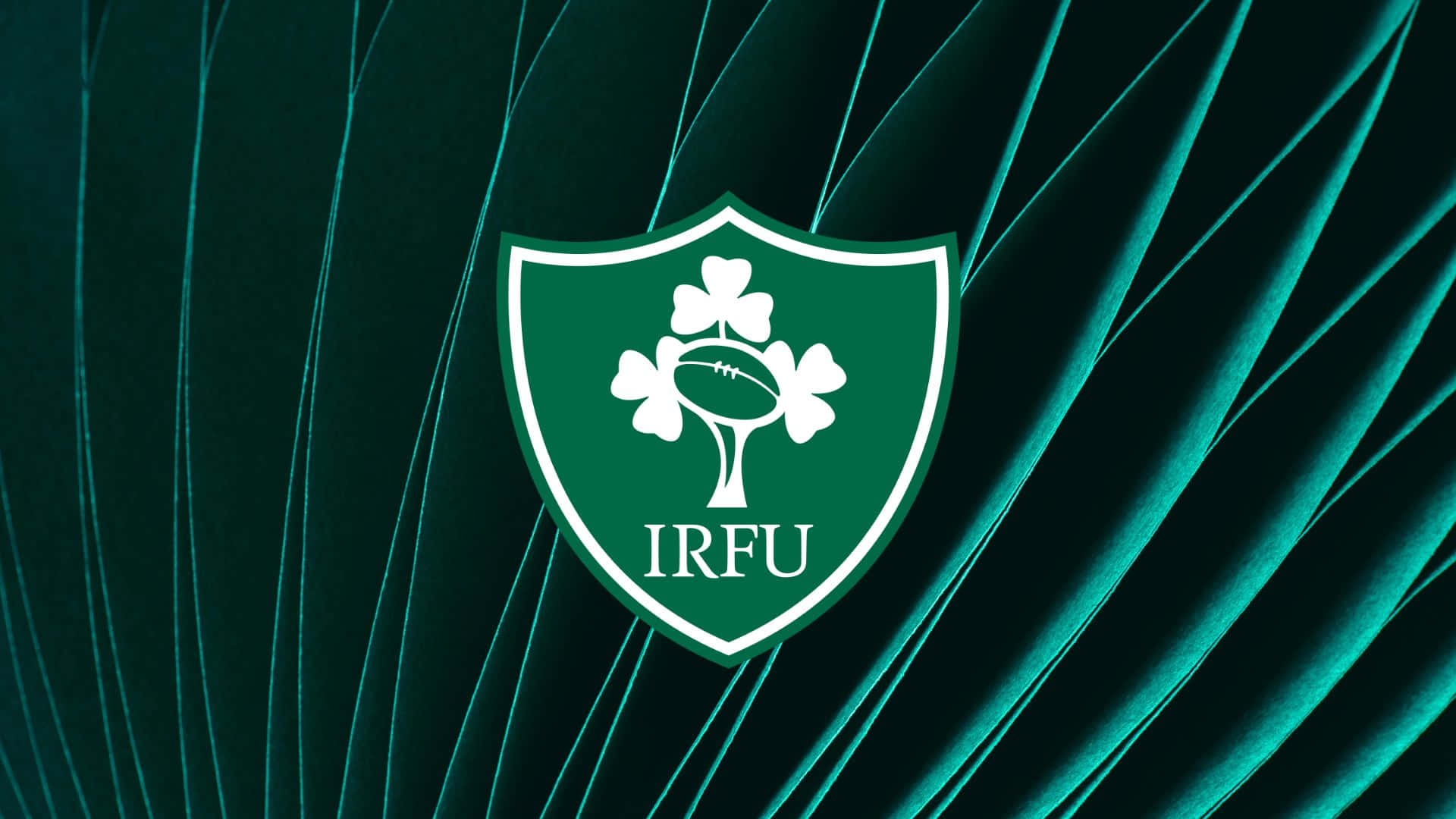Ireland Rugby 桌布 壁紙 — 一個白色的愛爾蘭橄欖球聯盟徽章，上面有三個三葉草和一個橄欖球，位於有紋理的青綠色天鵝絨背景中央。