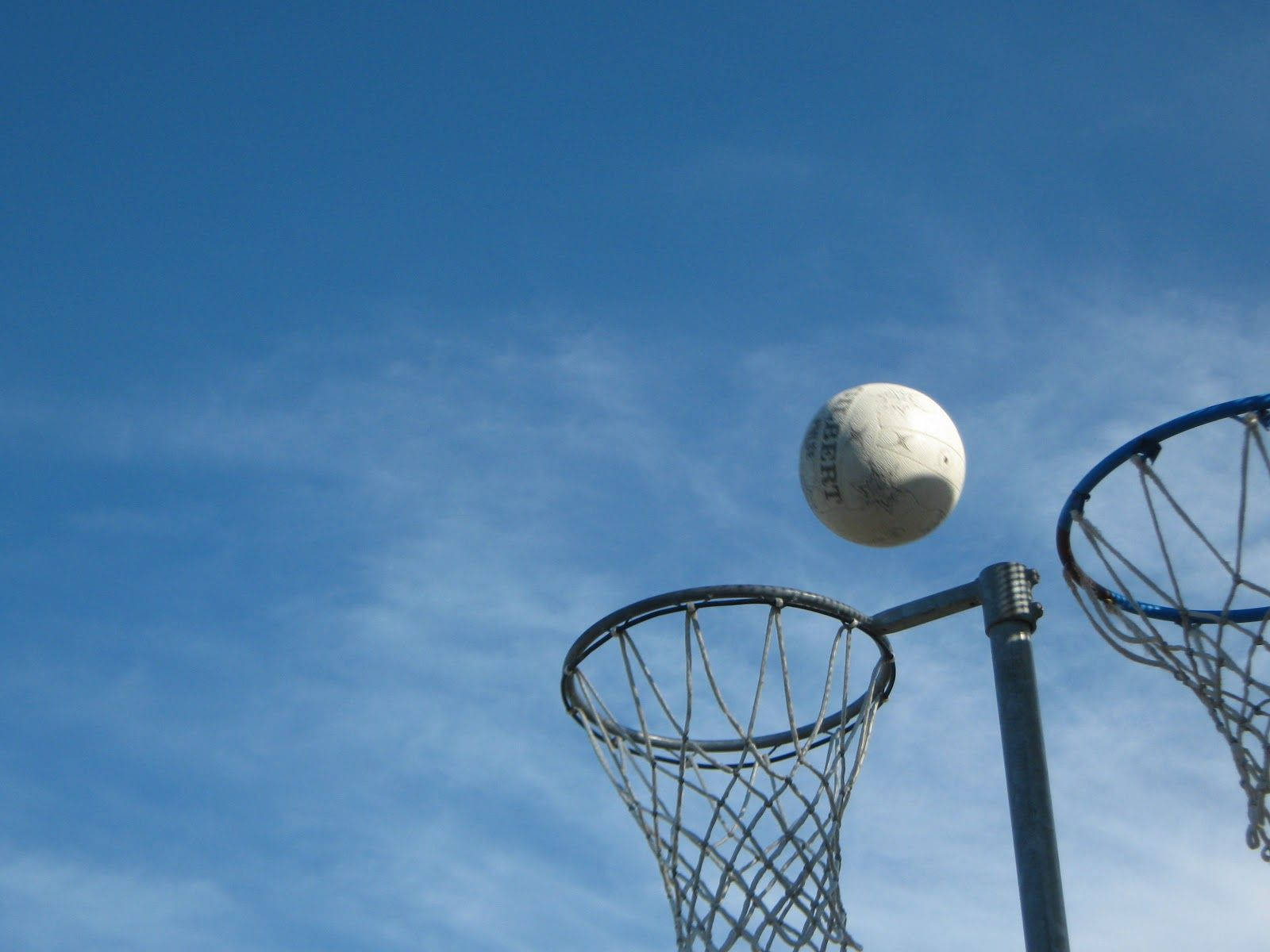 ball 桌布 壁紙 — 一個白色的網球在金屬圈上方半空中懸浮，背景是晴朗的藍天和薄雲。
