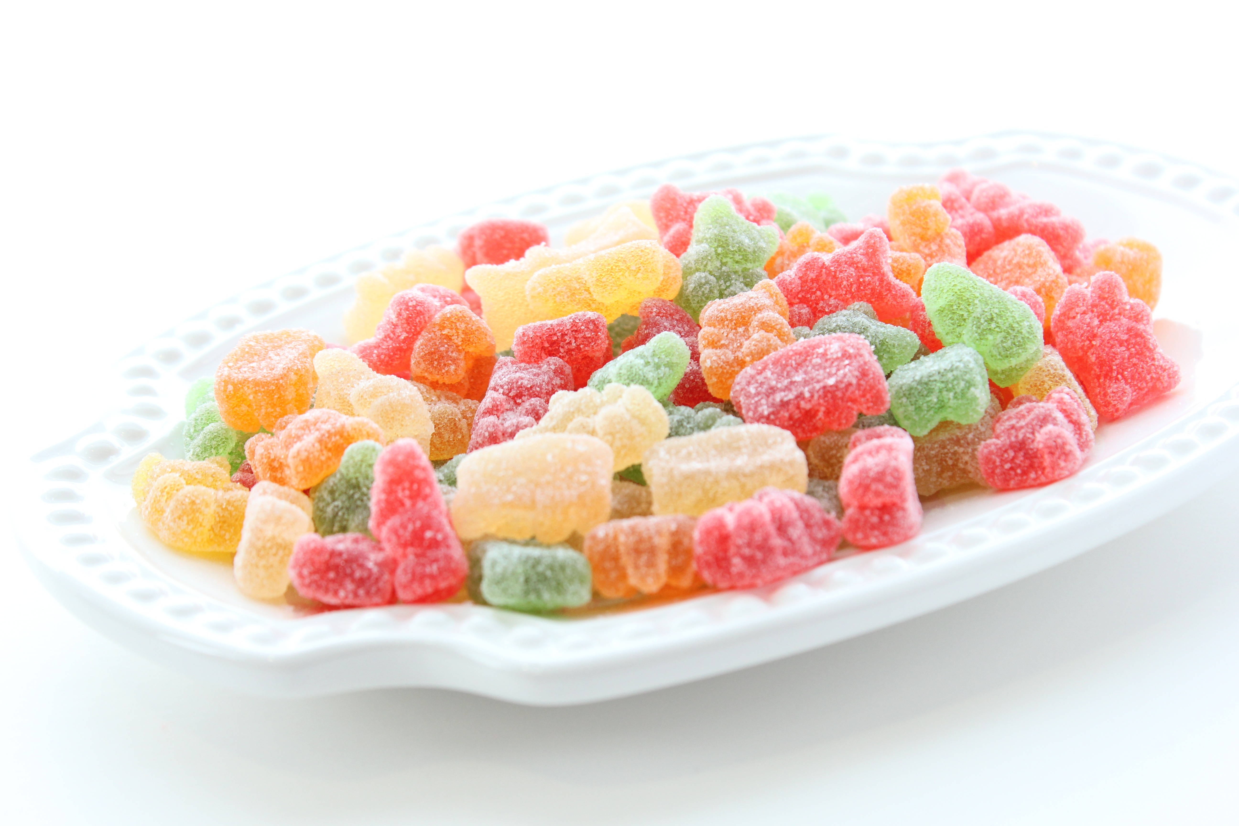 chewy 桌布 壁紙 — 一個白色盤子上堆滿了色彩繽紛、裹著糖晶的軟糖熊，背景是明亮的白色。