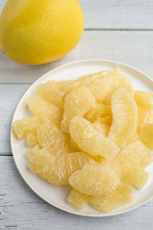 Fruits 桌布 壁紙 — 一個白色盤子上堆滿多汁的淡黃色柚子瓣，旁邊放著一個完整的柚子，置於經風化的白色木質表面上。