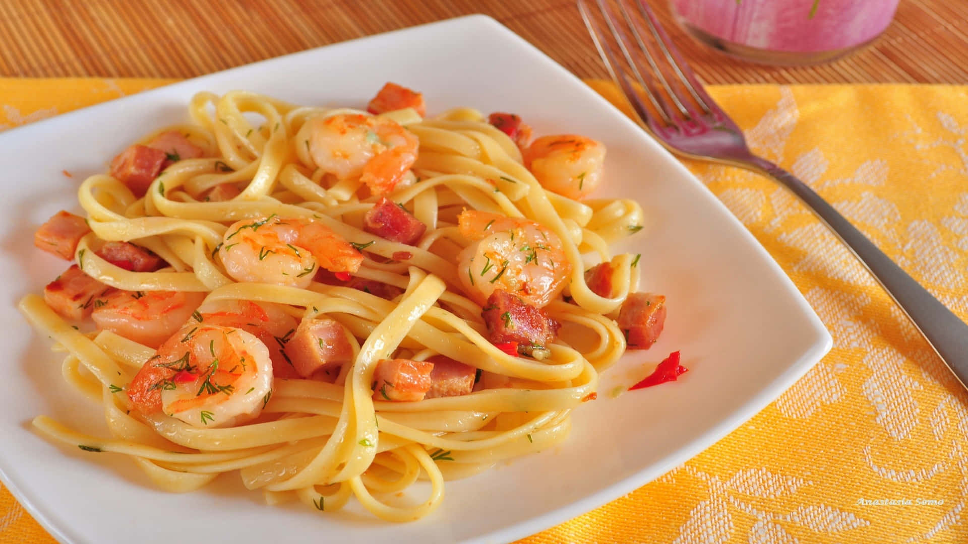 1920x1080 Pasta 桌布 壁紙 — 一個白色盤子上放滿了義大利寬麵，上面鋪滿了多汁的蝦和培根丁，放在鮮黃色圖案布上。