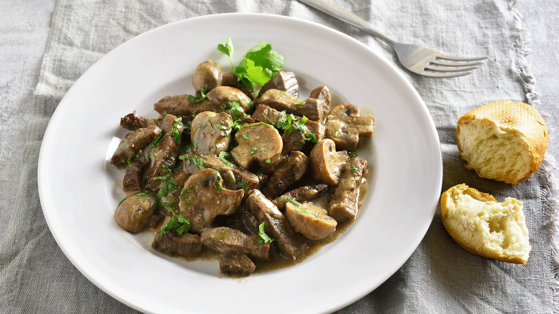 mushrooms 桌布 壁紙 — 一個白色盤子上放著嫩滑的牛肉斯特羅加諾夫配蘑菇和新鮮歐芹，旁邊有撕開的麵包放在亞麻布上。
