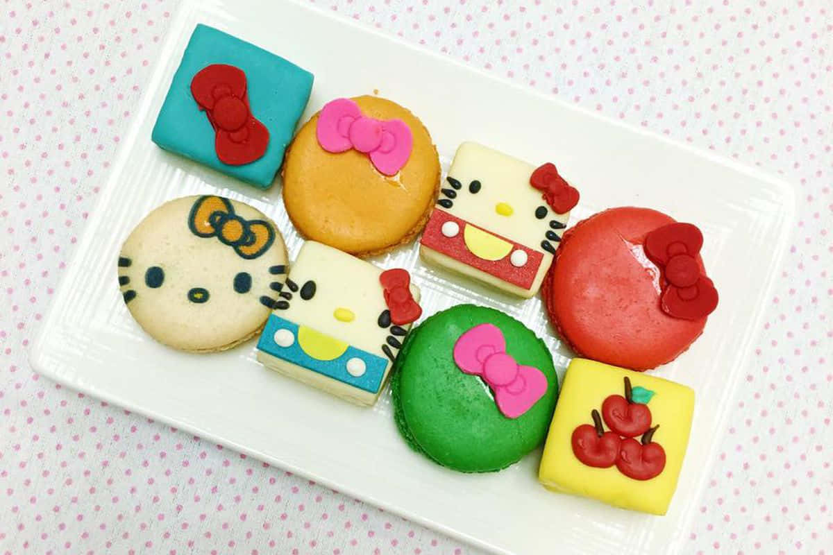 Hello Kitty 桌布 壁紙 — 一個白色盤子上放著色彩繽紛的Hello Kitty主題馬卡龍和餅乾，下面墊著粉紅色圓點布。
