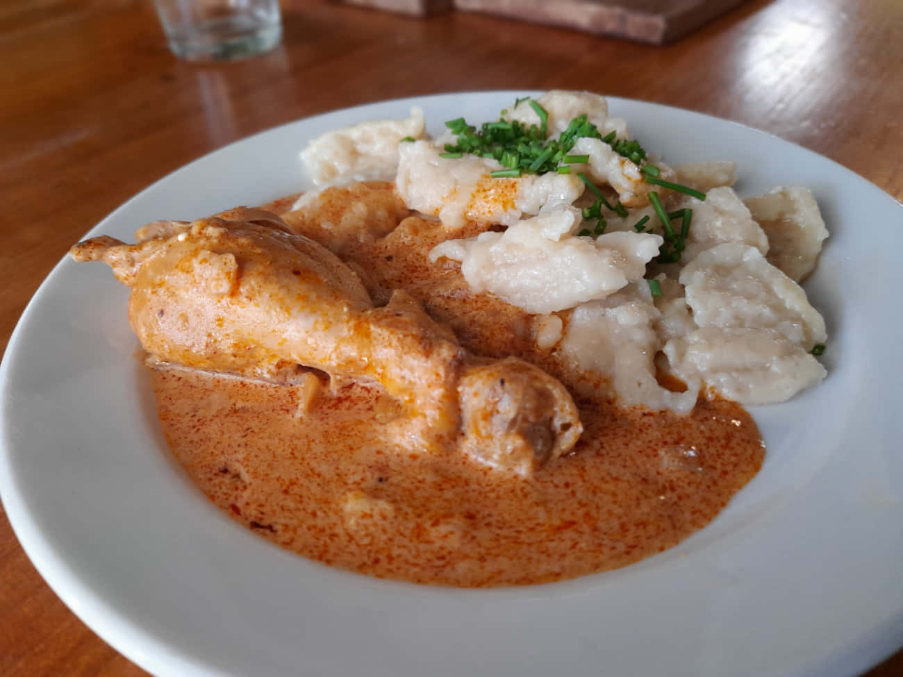 Chicken 桌布 壁紙 — 一個白色盤子盛裝奶油橙色咖哩雞肉和餃子，上面用新鮮綠色香草裝飾，放在木桌上。