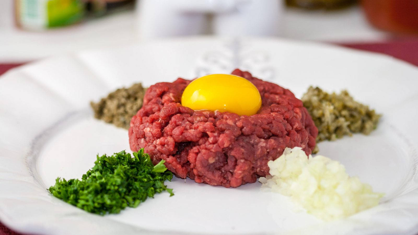 meat 桌布 壁紙 — 一個白色盤子盛裝生牛肉塔塔，中央放有鮮黃色蛋黃，周圍綴以切碎的巴西里、酸豆和洋蔥。