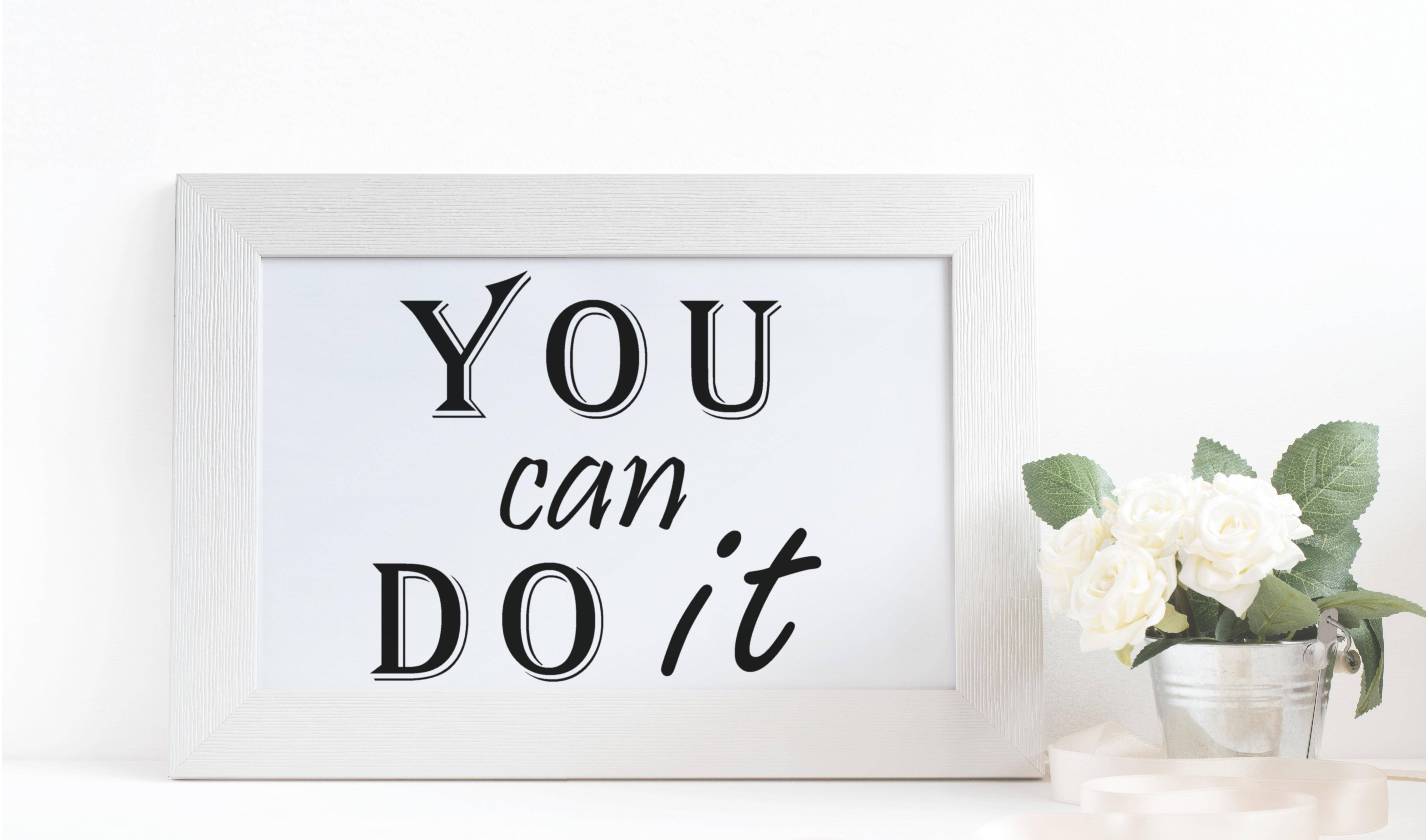 勵志動圖 桌布 壁紙 — 一個白色相框的勵志標語牌，上面寫著「YOU can DO it」，旁邊放著一桶白玫瑰，置於潔白的表面上。