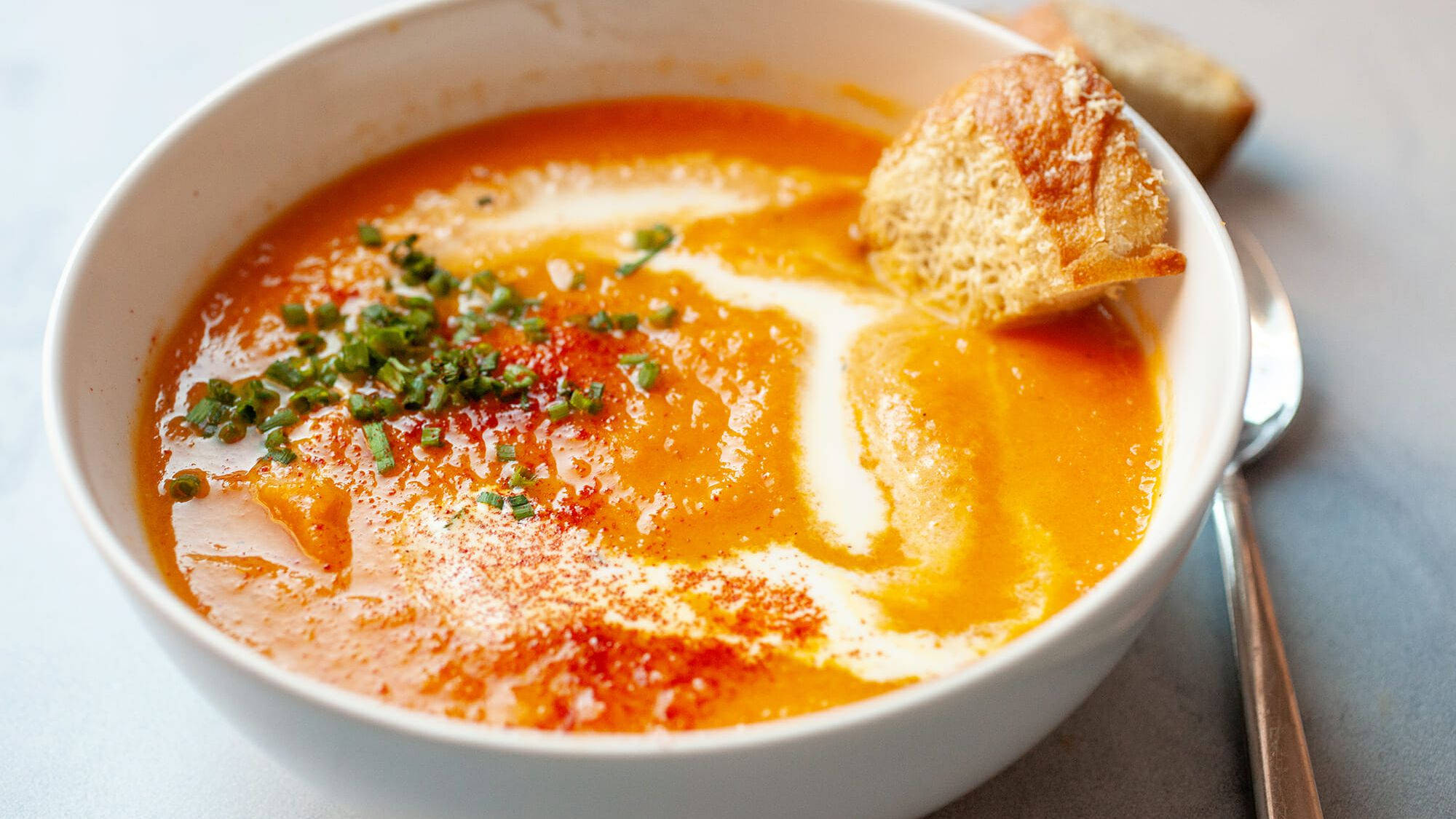 Chowder 桌布 壁紙 — 一個白色碗中的奶油橙色湯，飾以細香蔥和紅色香料，配以脆皮麵包丁。