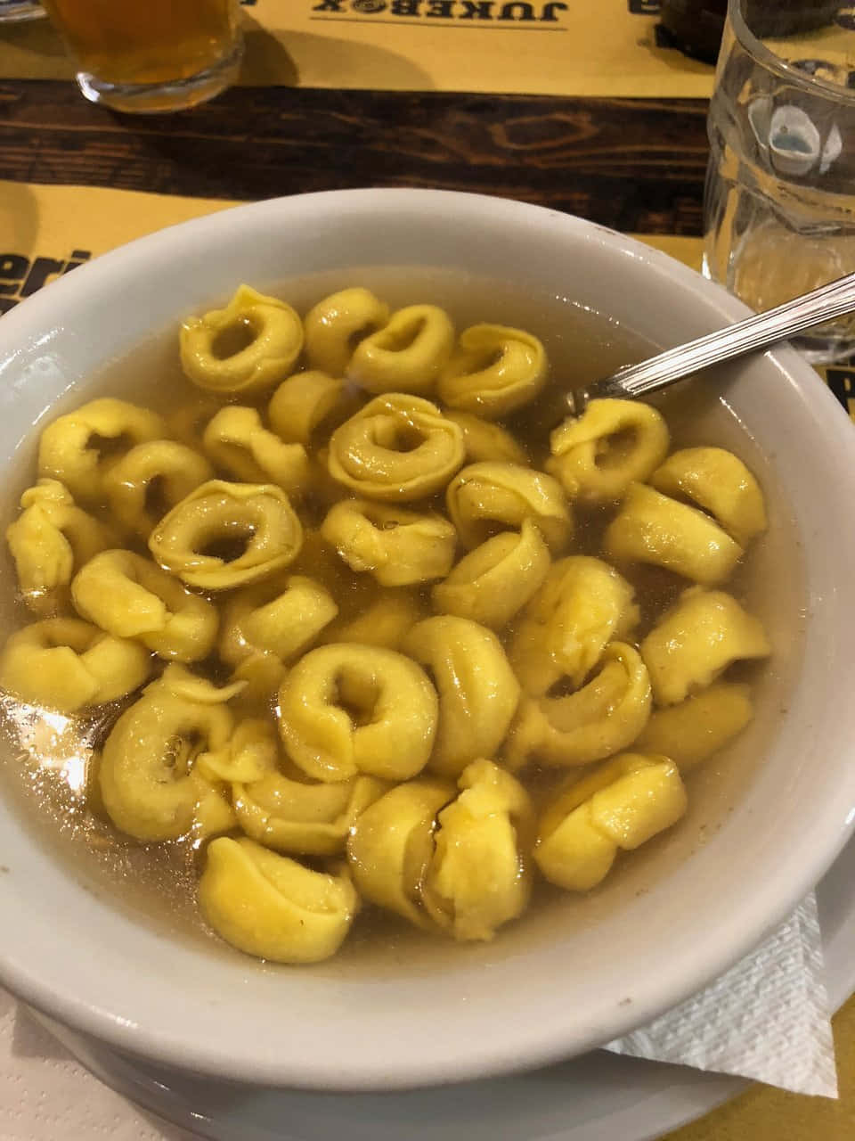 Pasta 桌布 壁紙 — 一個白色碗的特寫，裡面盛滿了金黃色的義大利餃子，浸泡在清澈的湯汁中，湯匙擱在碗內。