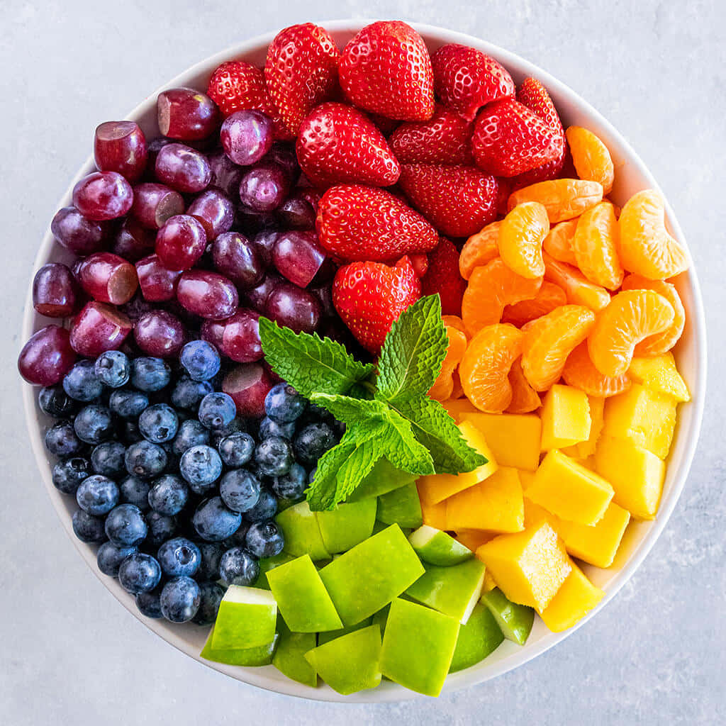 Fruit 桌布 壁紙 — 一個白色碗的鮮豔俯拍照片，裡面裝滿了色彩繽紛的切塊水果，排列成彩虹色塊。