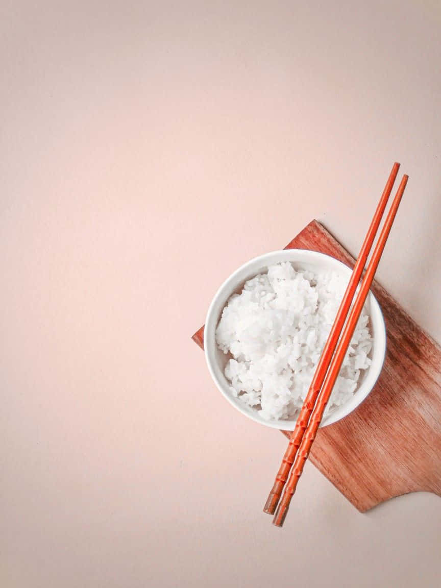 Minimalist Food 桌布 壁紙 — 一個白色碗盛裝 fluffy 蒸飯，搭配橙色筷子，放在木板上，背景是柔和蜜桃色。