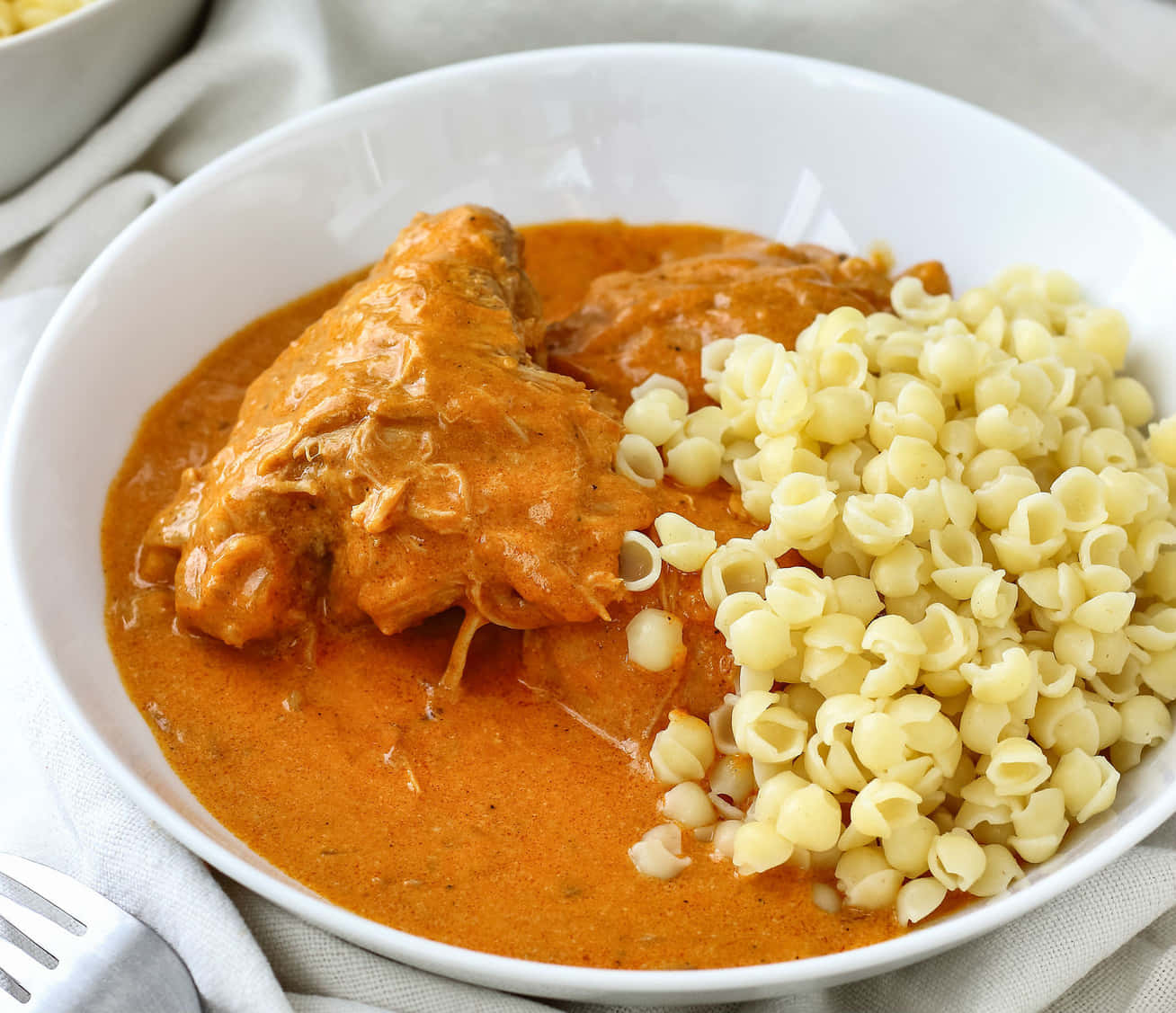 Chicken 桌布 壁紙 — 一個白色碗盛裝著嫩滑雞肉搭配濃郁橙醬，旁邊是奶油迪塔利尼義大利麵，放在亞麻餐巾上。