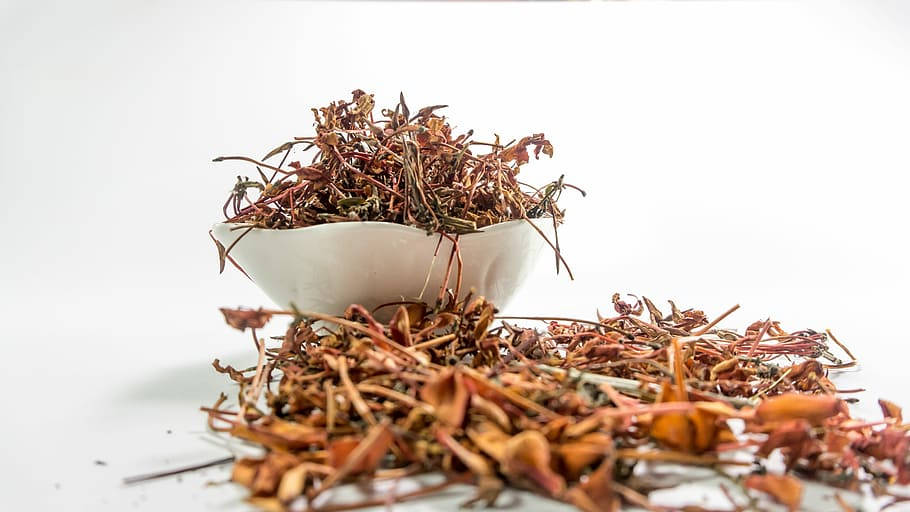 medicine 桌布 壁紙 — 一個白色碗裝滿了乾燥的紅褐色草藥，溢出到乾淨的白色表面上。