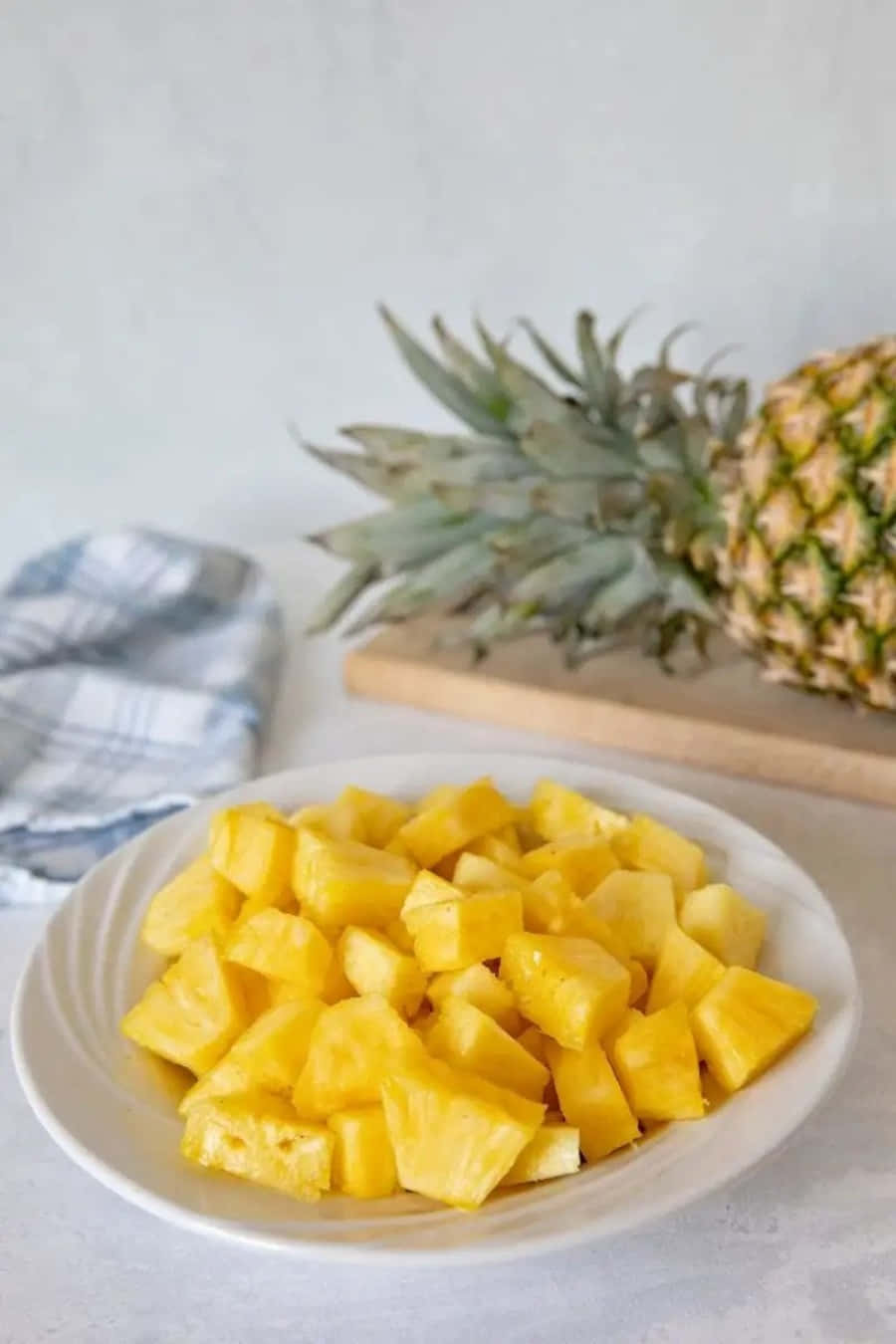 Pineapple 桌布 壁紙 — 一個白色碗裝滿多汁的黃色鳳梨塊，旁邊放著一個完整的鳳梨在木板上。