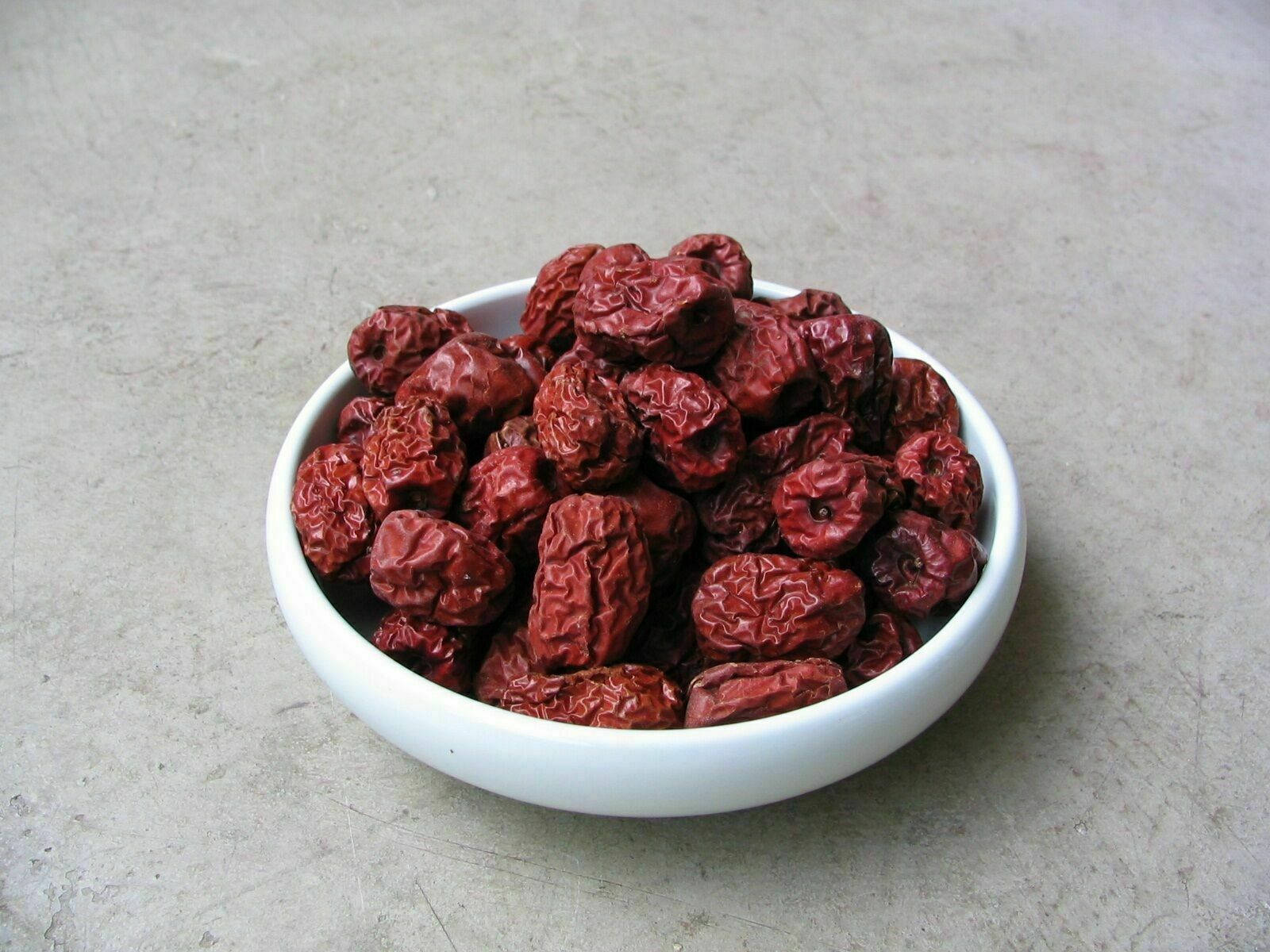 Fruits 桌布 壁紙 — 一個白色碗裝滿皺巴巴的深紅色乾紅棗，放在中性灰色紋理表面上。