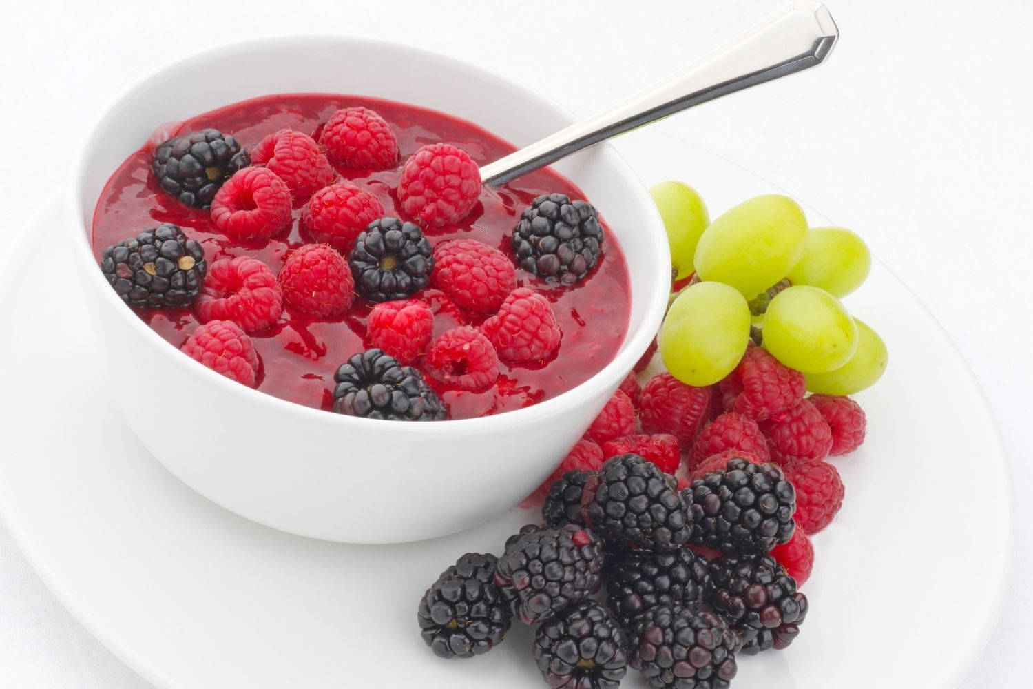 Berry 桌布 壁紙 — 一個白色碗裝滿鮮豔的紅色莓果冰沙，上面放上新鮮的覆盆子和黑莓，旁邊有青葡萄。