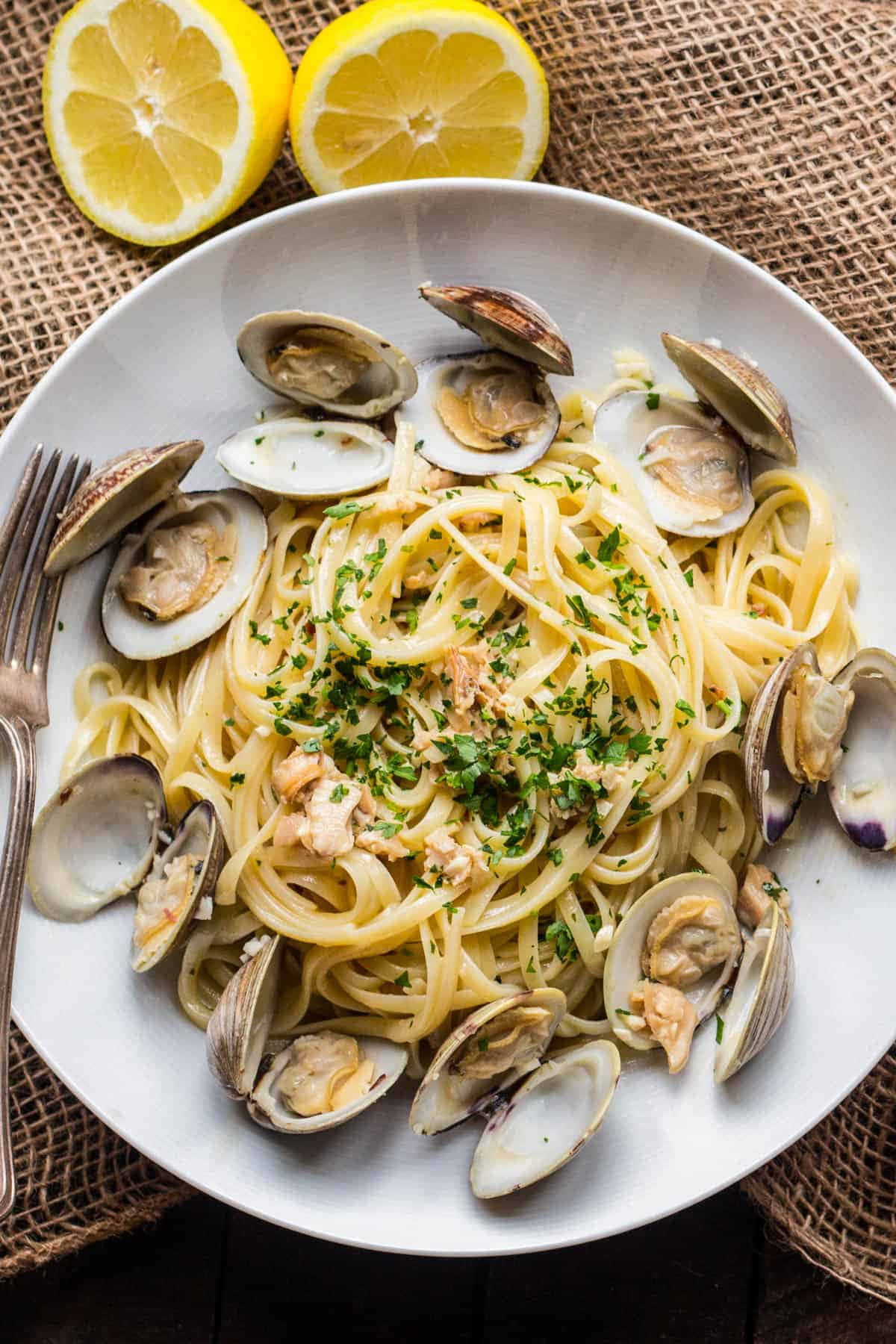 Clam 桌布 壁紙 — 一個白色碗裝著奶油蛤蜊義大利麵，飾以巴西里和檸檬半個，放在麻布表面上。