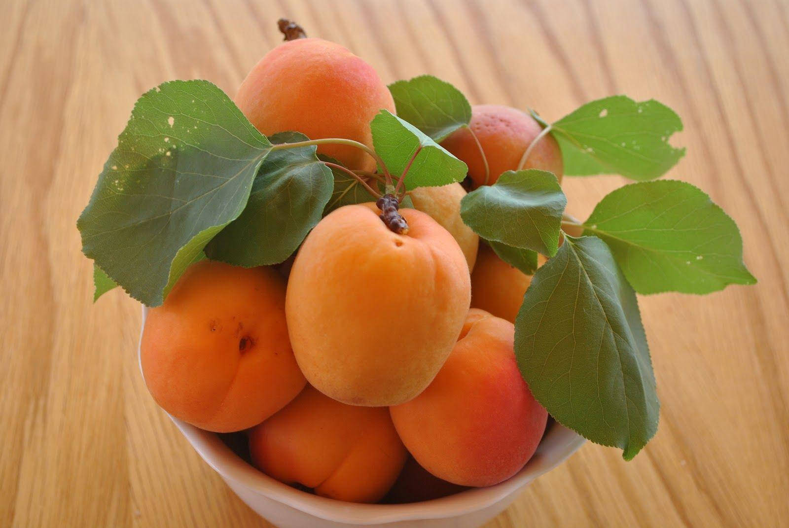 Fruits 桌布 壁紙 — 一個白色碗裡盛滿新鮮杏子和綠葉，放在淺色木質表面上。