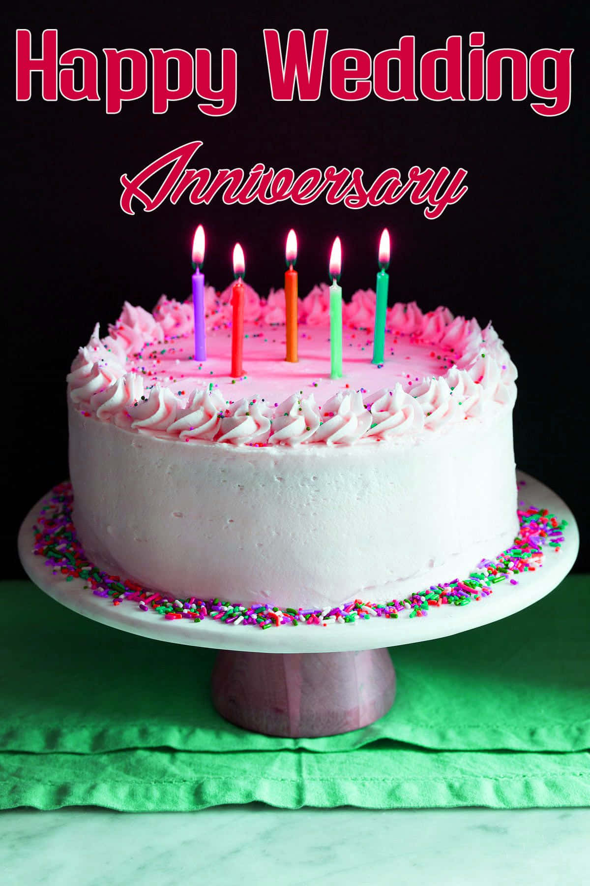Anniversary 桌布 壁紙 — 一個白色糖霜蛋糕，帶有粉紅色漩渦和彩色糖粒，上面放著五根點燃的蠟燭和「Happy Wedding Anniversary」文字。
