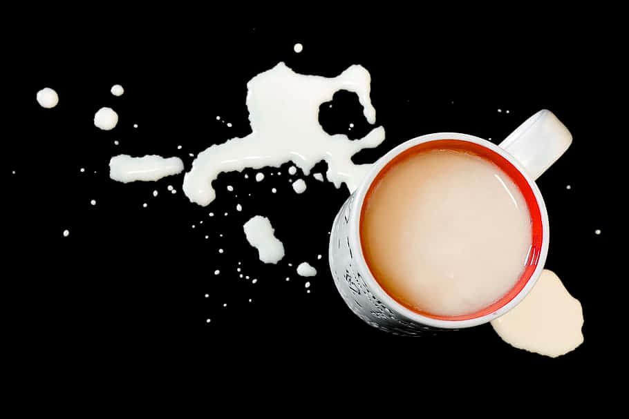 Milk And Coffee 桌布 壁紙 — 一個白色紅邊的馬克杯將奶油狀液體灑在純黑表面上，形成動態的飛濺和滴落。