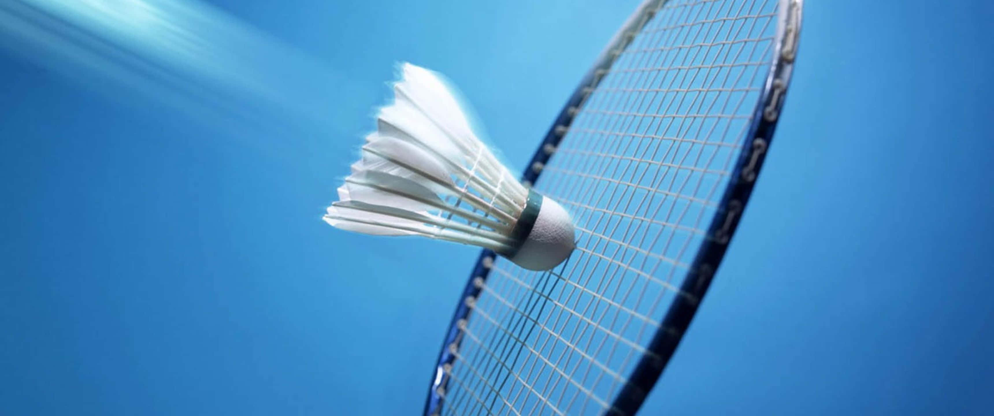3440x1440p Badminton 桌布 壁紙 — 一個白色羽毛球在充滿活力的藍天背景下，捕捉到即將擊中羽毛球拍的瞬間動態。