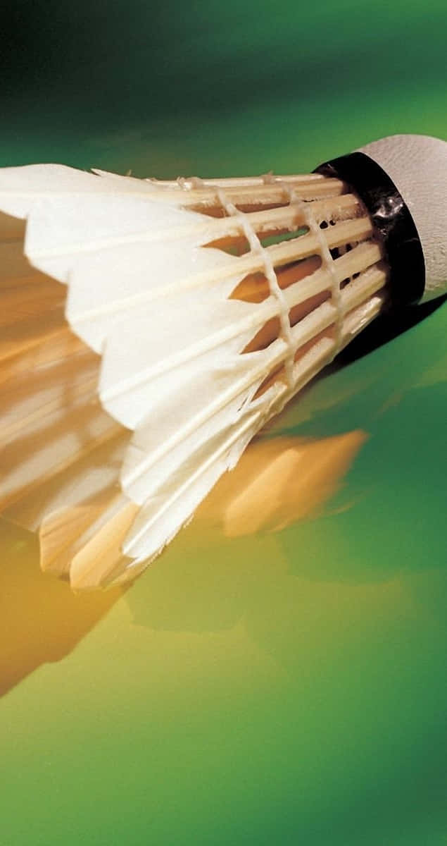 Shuttlecock 桌布 壁紙 — 一個白色羽毛羽毛球在充滿活力的綠色和黃色模糊背景中運動的特寫。