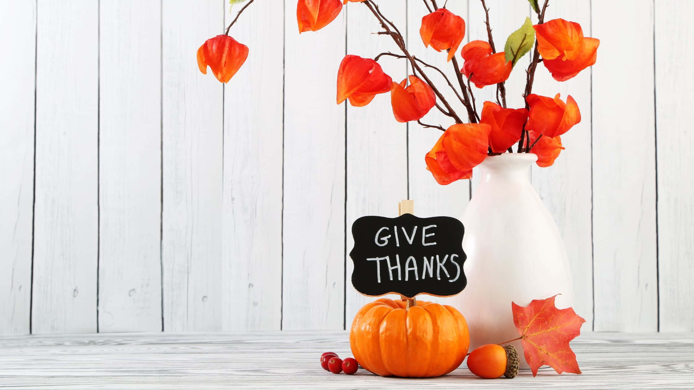 Thanksgiving Desktop 桌布 壁紙 — 一個白色花瓶，插著橙色花朵和一個小南瓜，放在木桌上，旁邊有一塊寫著 give thanks 的黑板。