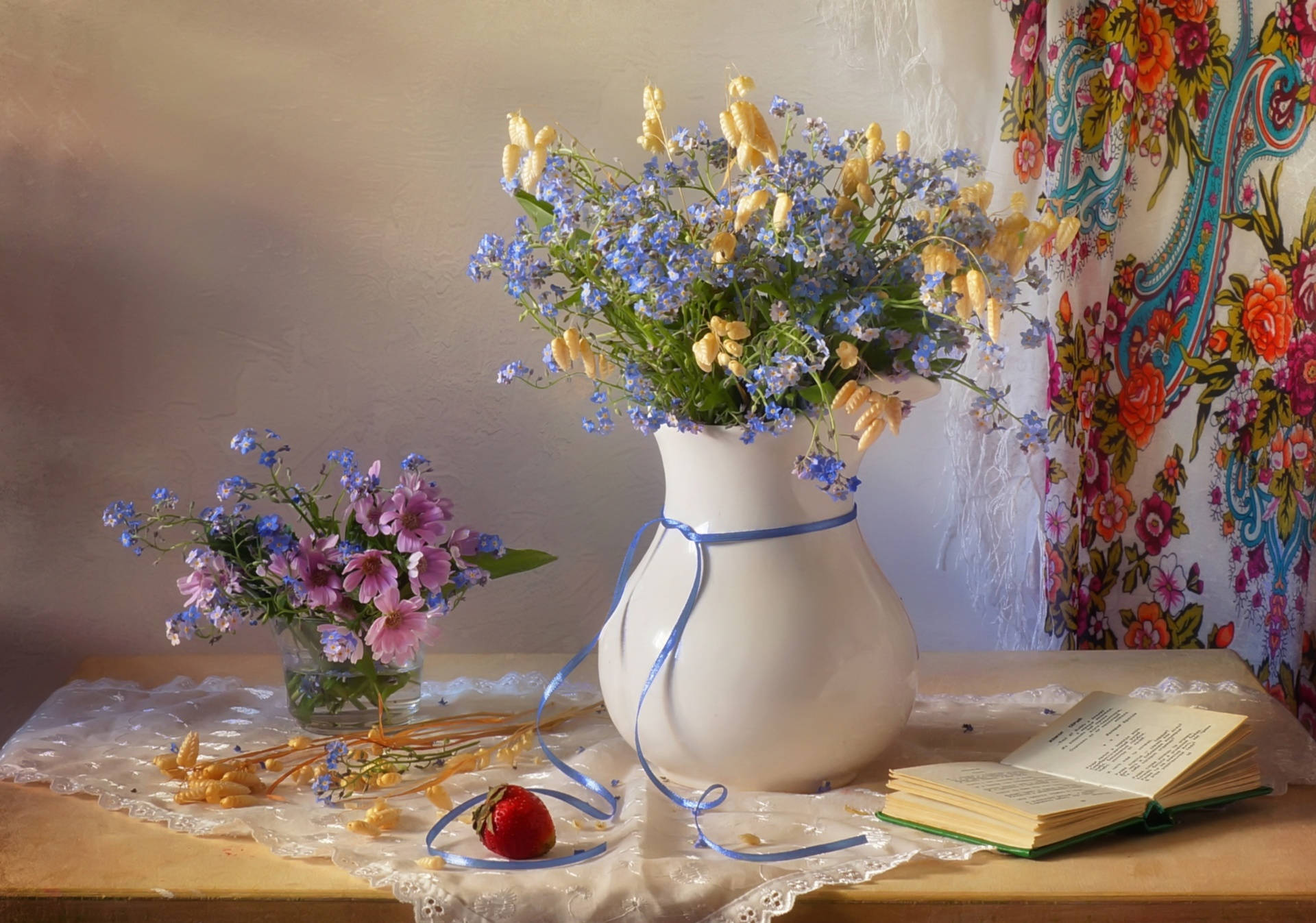 Pinterest 美學 桌布 壁紙 — 一個白色花瓶裝滿藍色和黃色的花朵，放在鋪有蕾絲的桌子上，旁邊有草莓、一本打開的書和一個較小的花卉佈置。