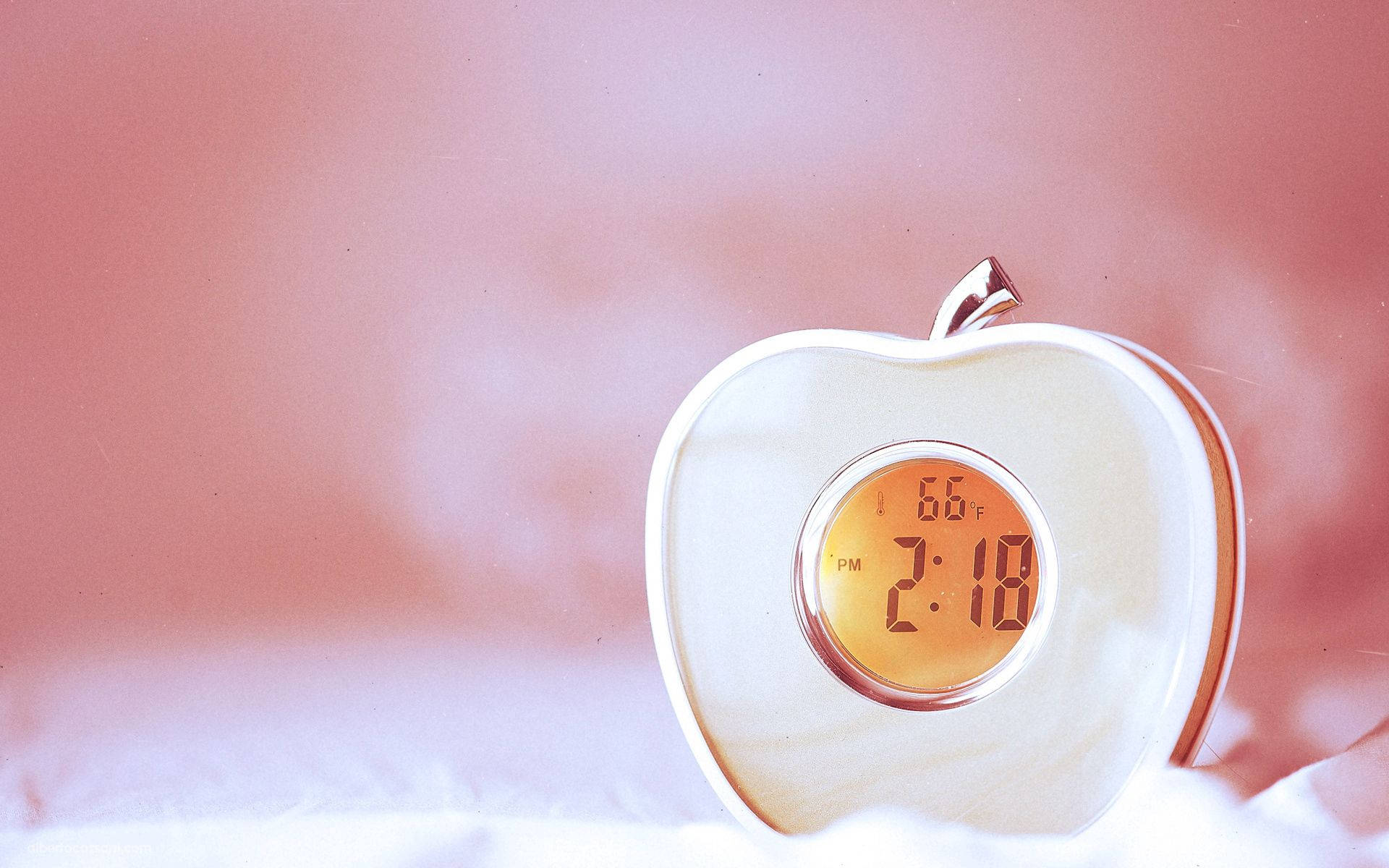 Clock 桌布 壁紙 — 一個白色蘋果形狀的數位時鐘顯示下午2:18和華氏66度，放置在柔軟的白色表面上，背景為粉紅色漸變。