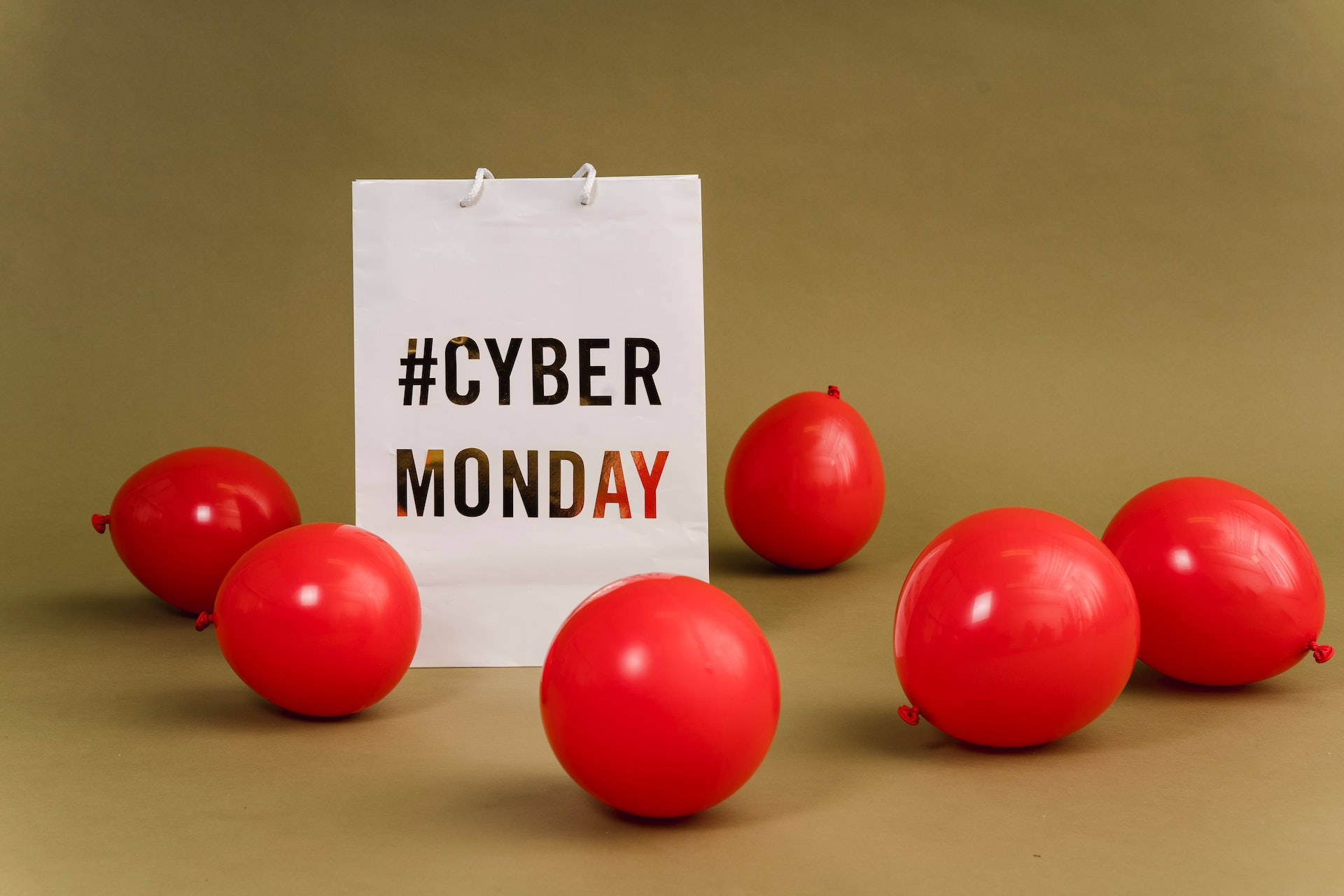 紅色動圖 桌布 壁紙 — 一個白色購物袋，上面標有 #CYBER MONDAY，周圍環繞著鮮紅色氣球，背景為柔和的棕色。
