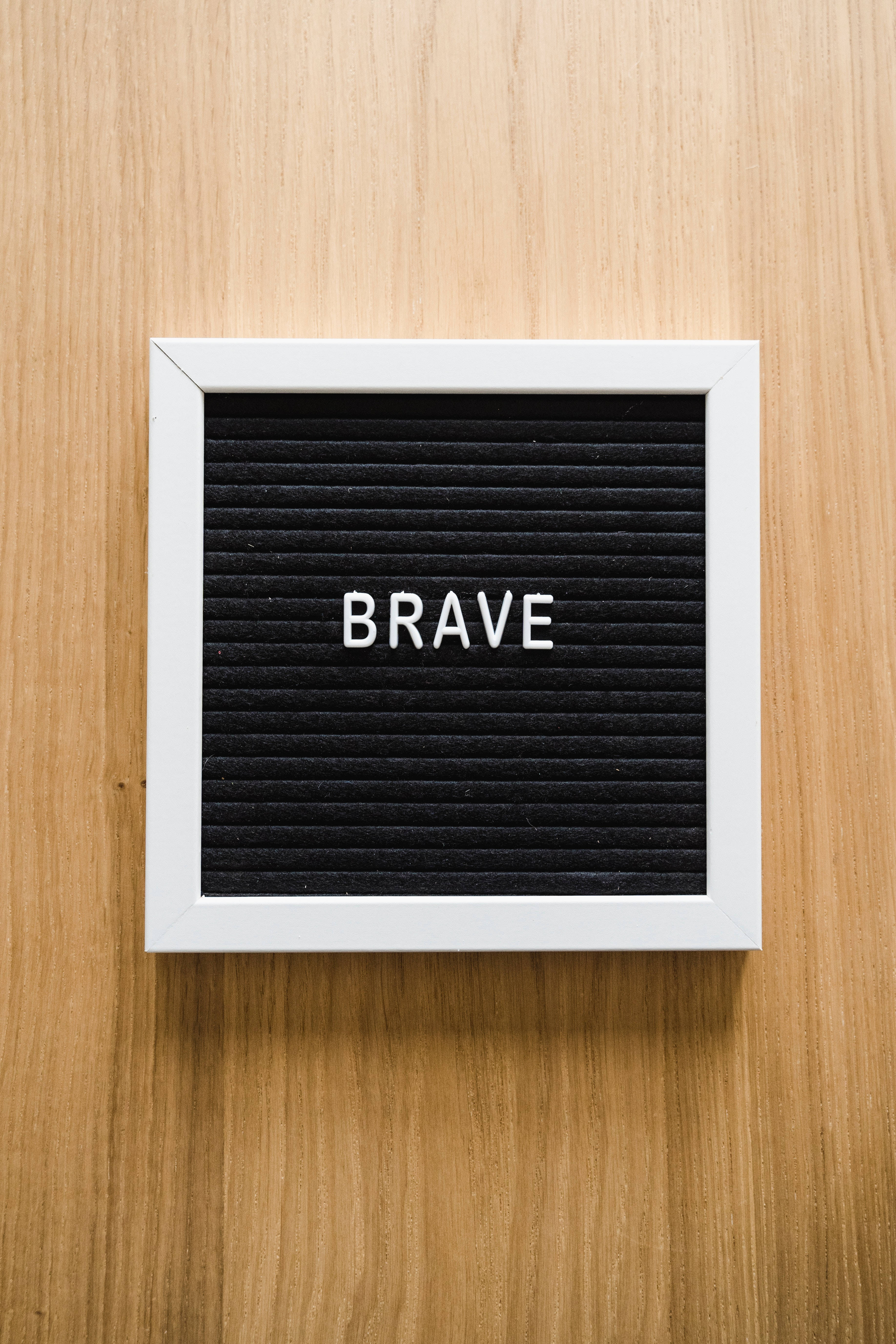 Brave 桌布 壁紙 — 一個白色邊框的字母板，在黑色絨布上用白色字母顯示BRAVE這個詞，放置在淺色木質表面上。