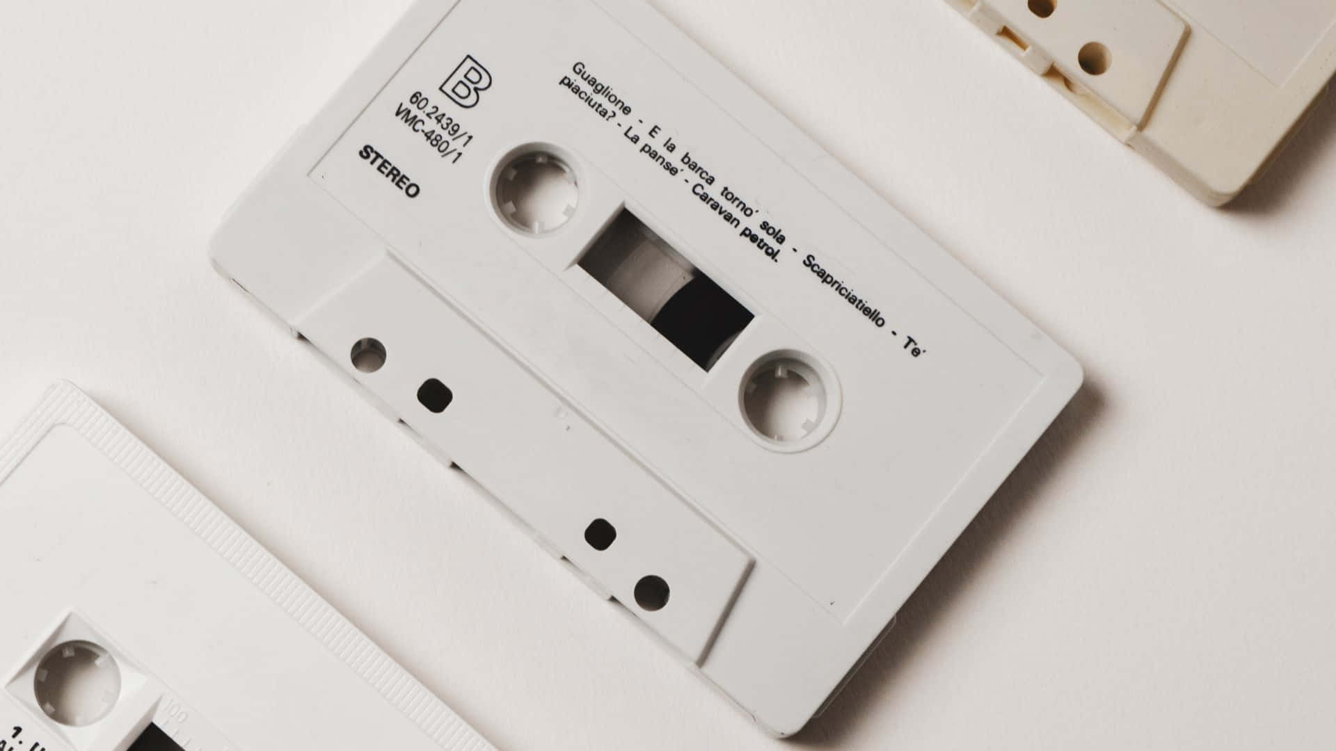 音樂美學 桌布 壁紙 — 一個白色錄音帶，帶有可見的曲目標籤，放在純白色表面上，喚起對類比音樂的懷舊感。