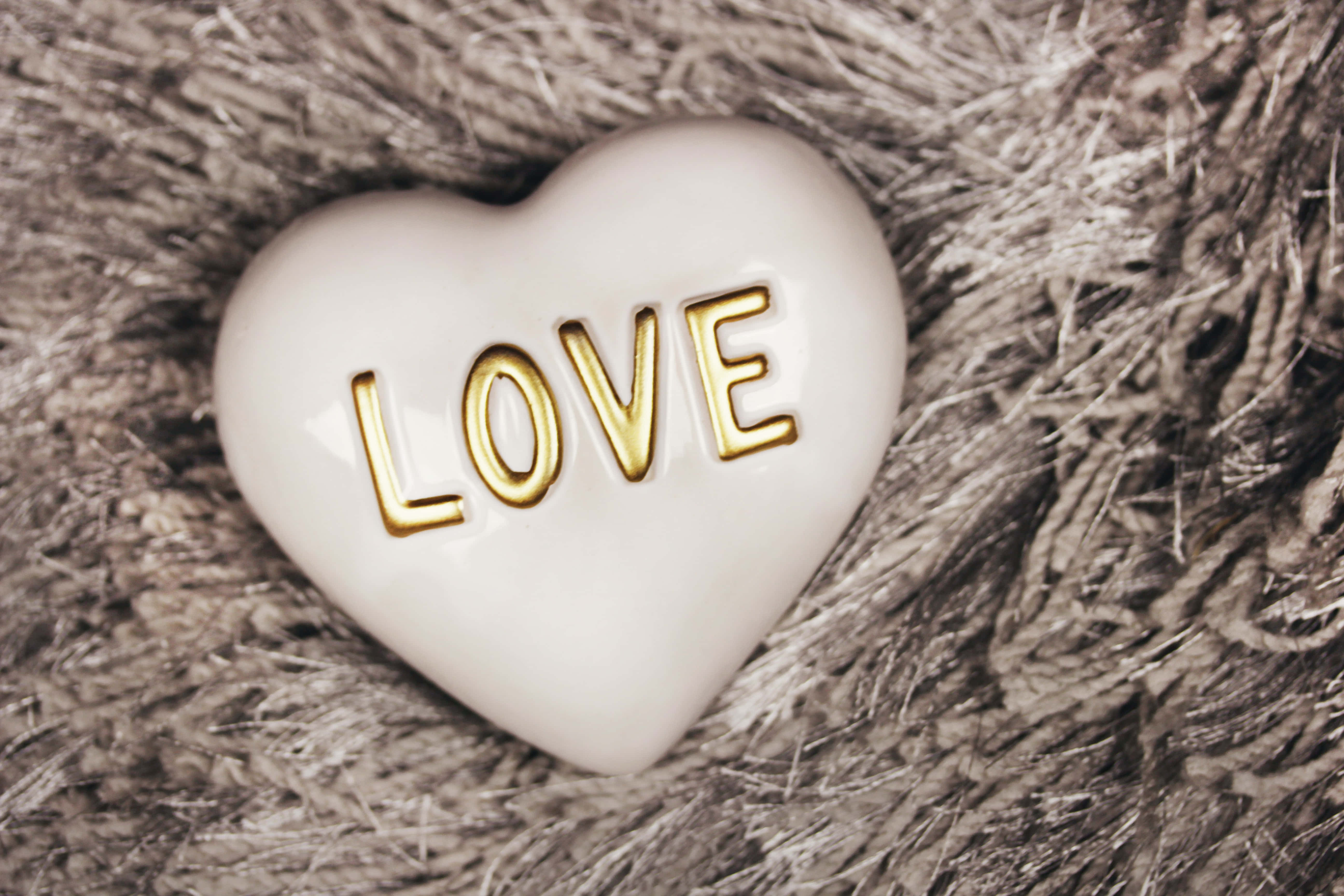 White Heart 桌布 壁紙 — 一個白色陶瓷心形，上面有金色壓印字母拼出 love，放置在質感豐富的棕色編織布料上。
