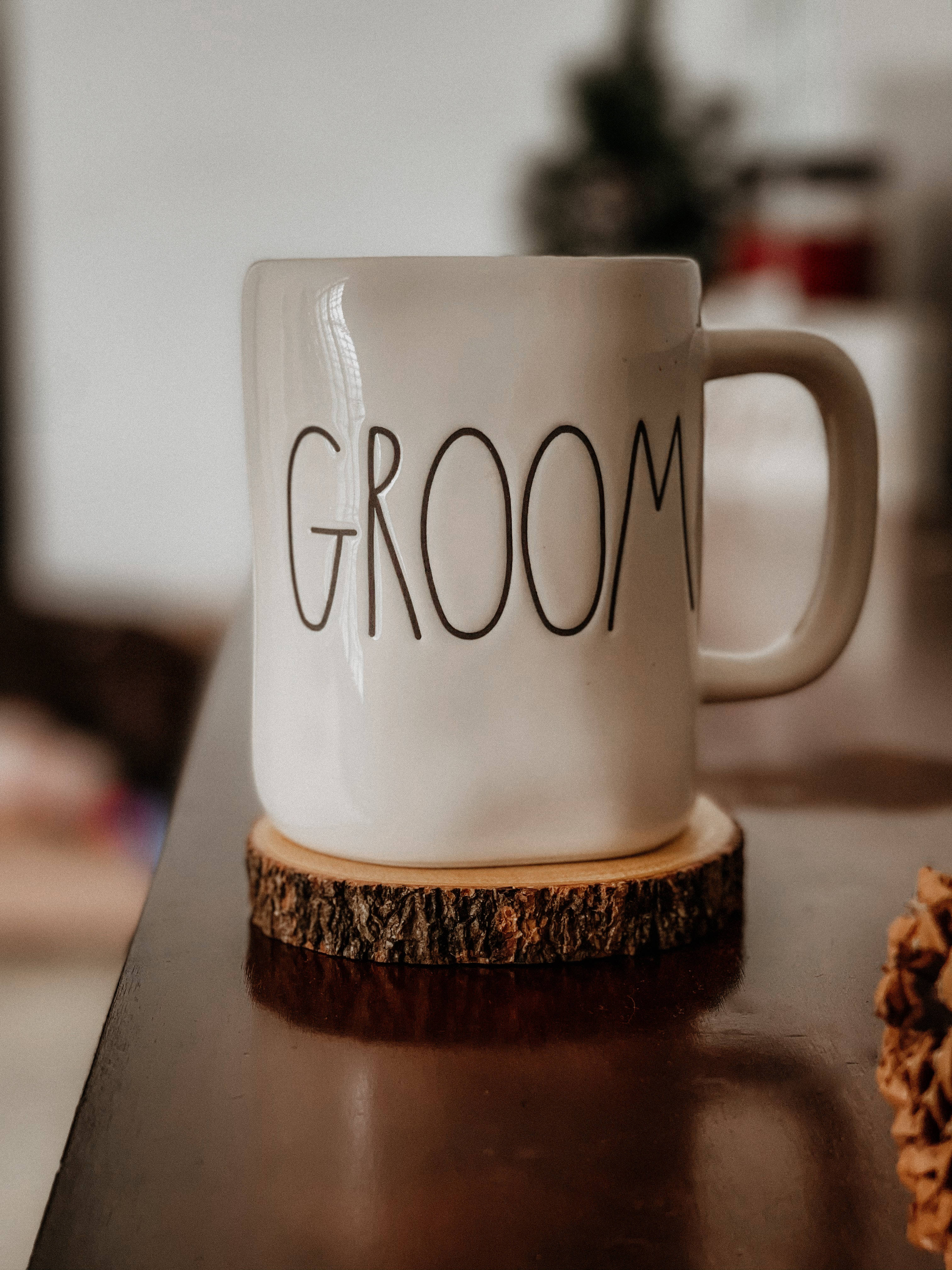 Groom 桌布 壁紙 — 一個白色陶瓷杯，上面標有「GROOM」，放在深色桌子上的質樸木杯墊上，背景柔和模糊。