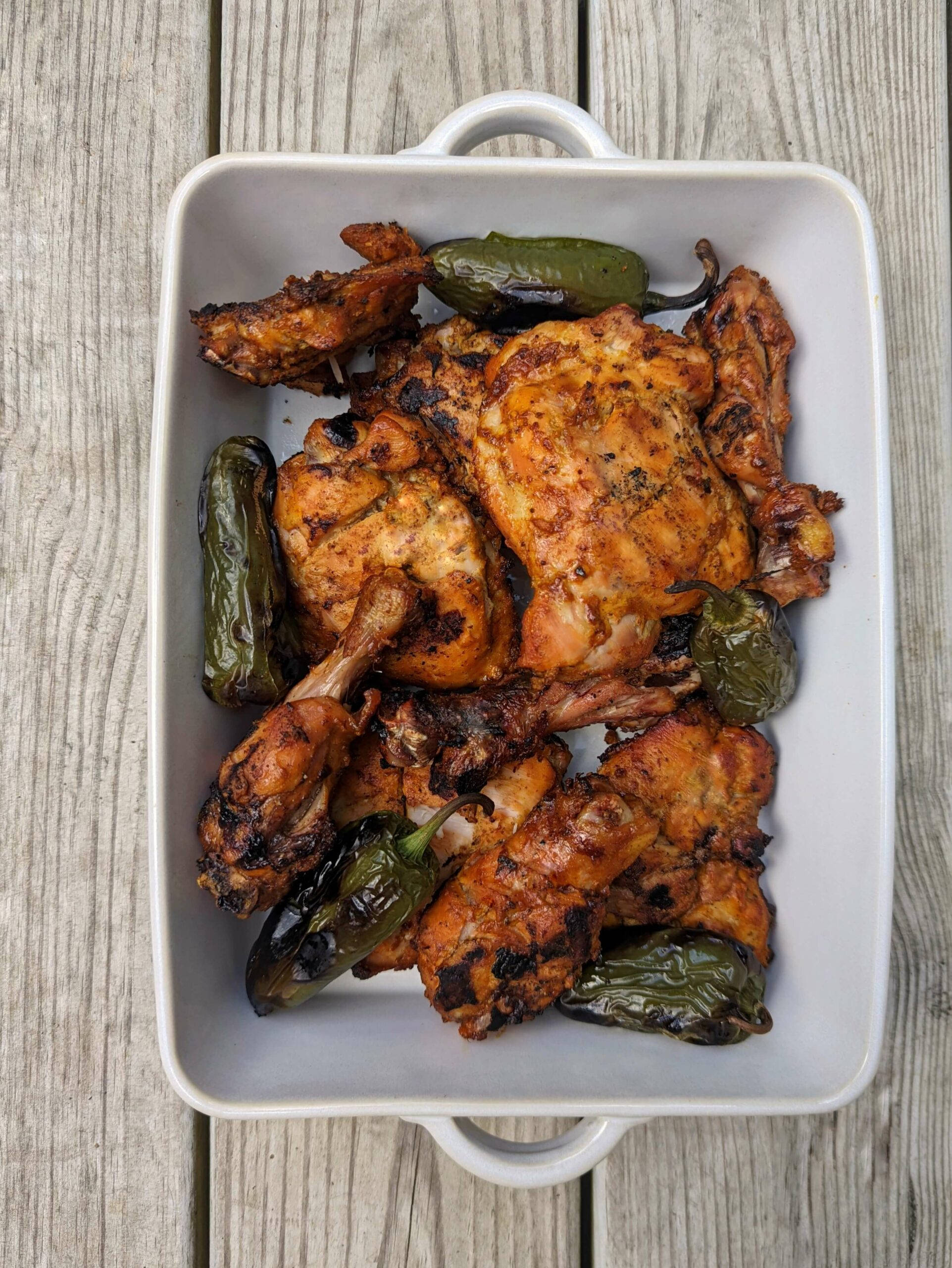 fried chicken 桌布 壁紙 — 一個白色陶瓷盤盛裝著烤雞塊和焦黑的青辣椒，放在風化的木質表面上。