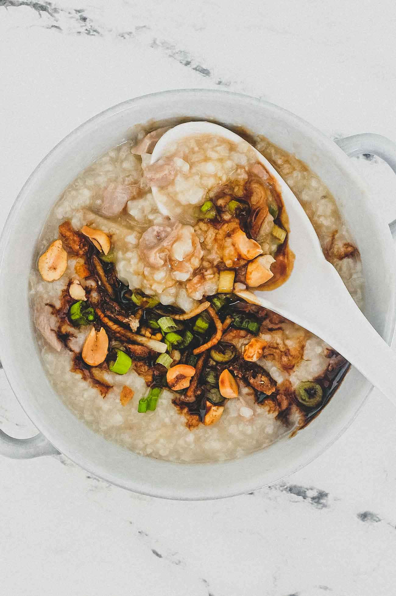 Food Photography 桌布 壁紙 — 一個白色陶瓷碗盛載著 creamy 的粥，上面有花生、青蔥和深色醬汁，湯匙舀起一勺。