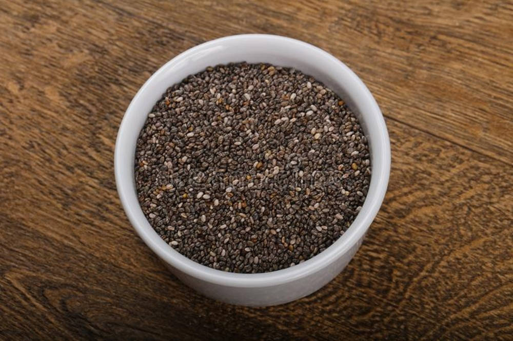 healthy 桌布 壁紙 — 一個白色陶瓷碗裝滿黑白奇亞籽，放在濃郁的棕色木質表面上。