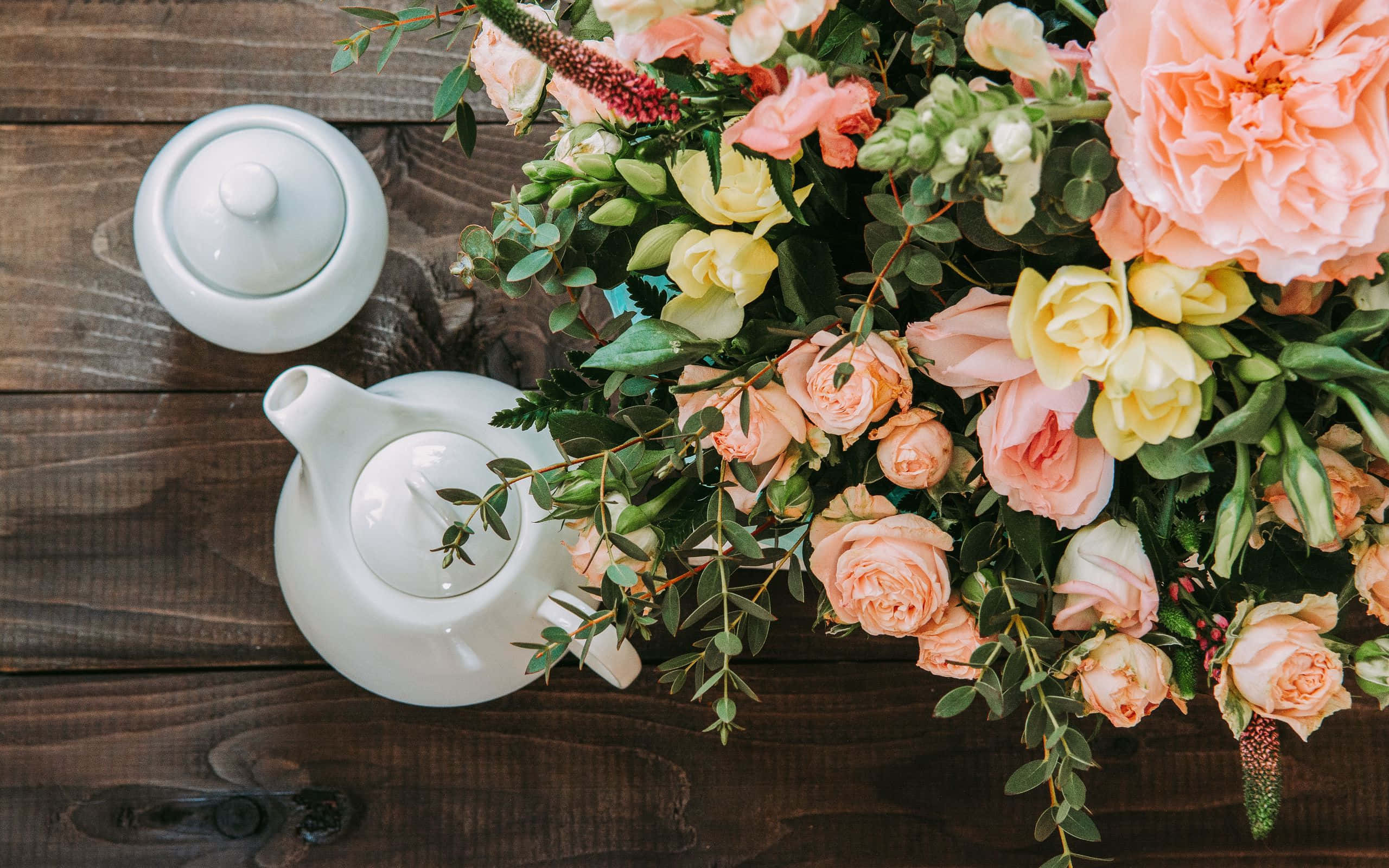Tea Party 桌布 壁紙 — 一個白色陶瓷茶壺和蓋子放在深色木桌上，旁邊是一束茂盛的蜜桃黃玫瑰和綠葉。
