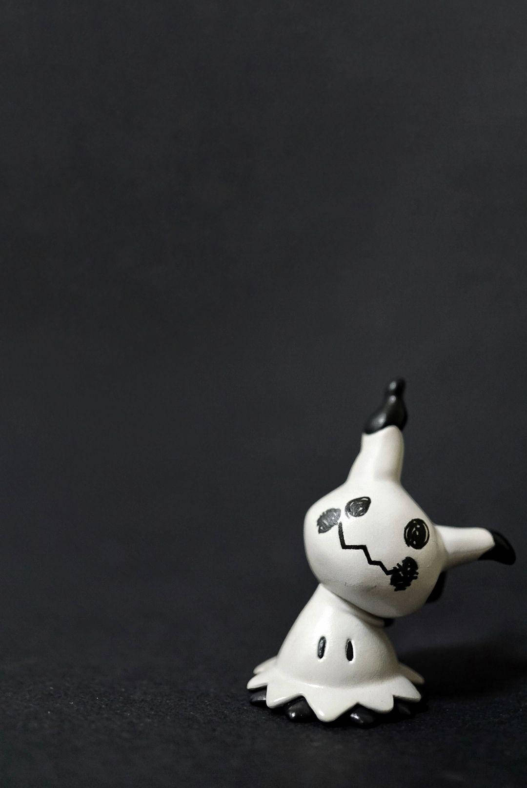 人像動態 桌布 壁紙 — 一個白色陶瓷鬼魂公仔，有黑色眼睛和鋸齒狀嘴巴，站在深色紋理背景前。