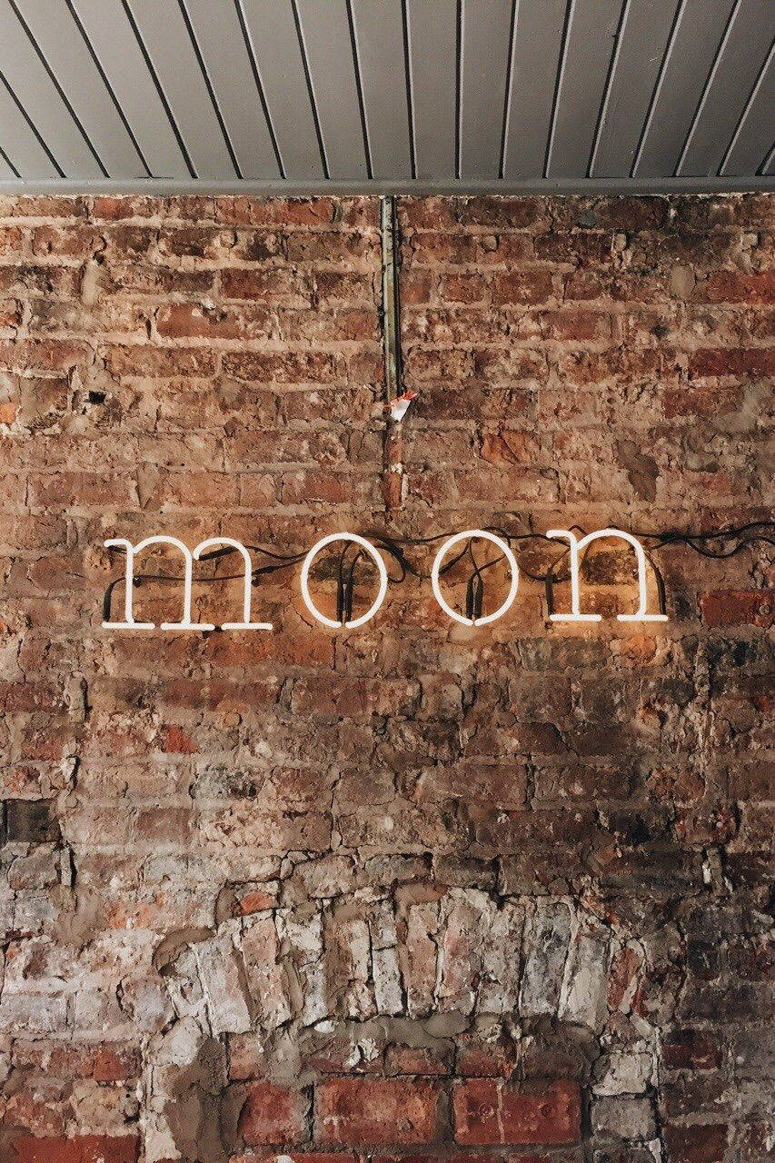 淺棕色美學動圖 桌布 壁紙 — 一個白色霓虹燈牌拼出moon，在金屬天花板下的風化磚牆上發光。