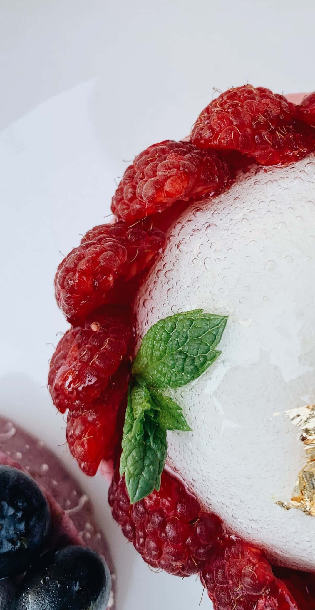 Pixel 3 Desserts 桌布 壁紙 — 一個白色霜糖甜點的特寫，上面裝飾著新鮮的紅覆盆子和一片綠色薄荷葉，放在白色盤子上。