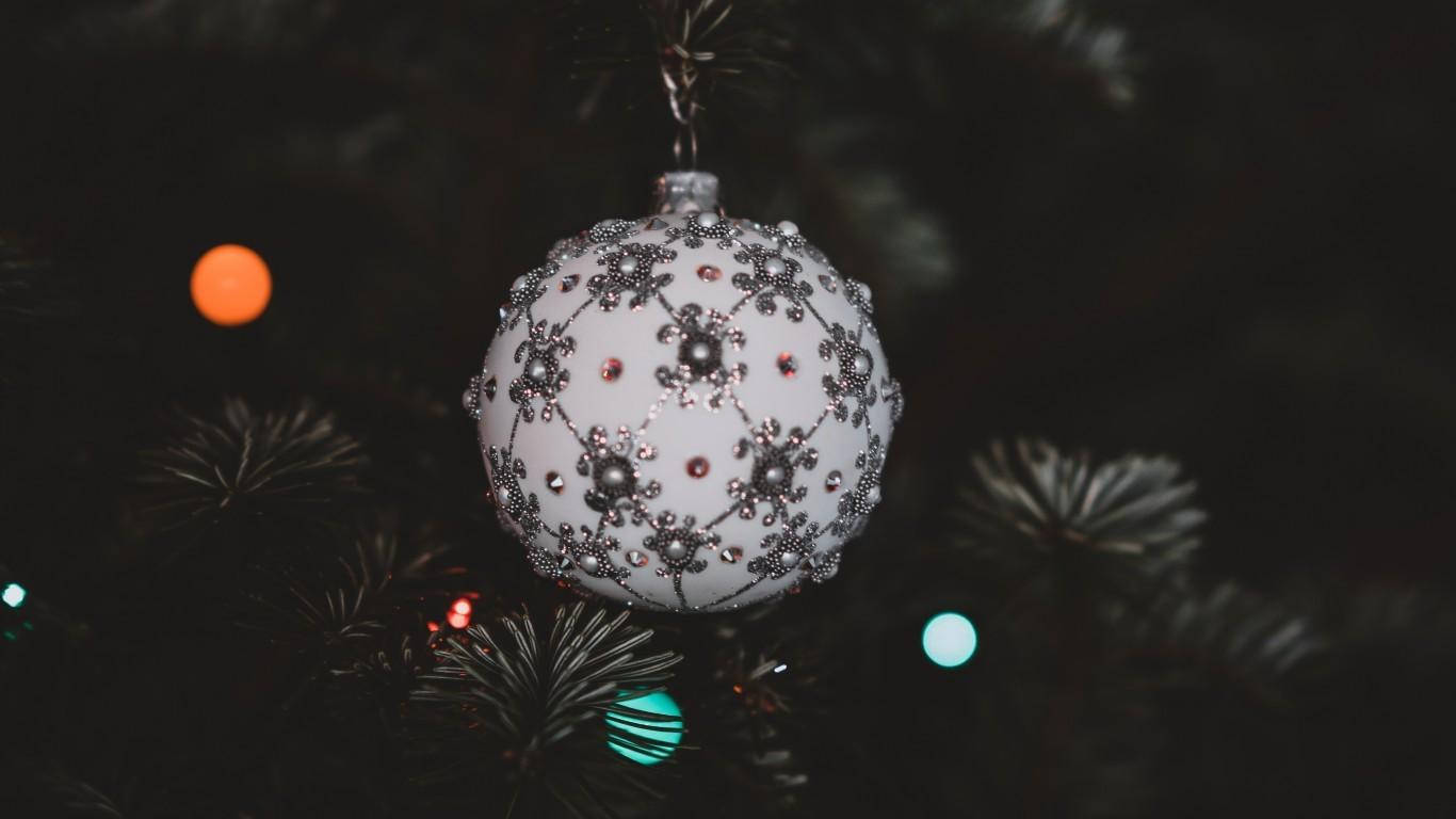 christmas laptop 桌布 壁紙 — 一個白色飾品，帶有銀色和紅色的閃亮雪花，掛在昏暗的松樹上，樹上有模糊的彩色燈光。