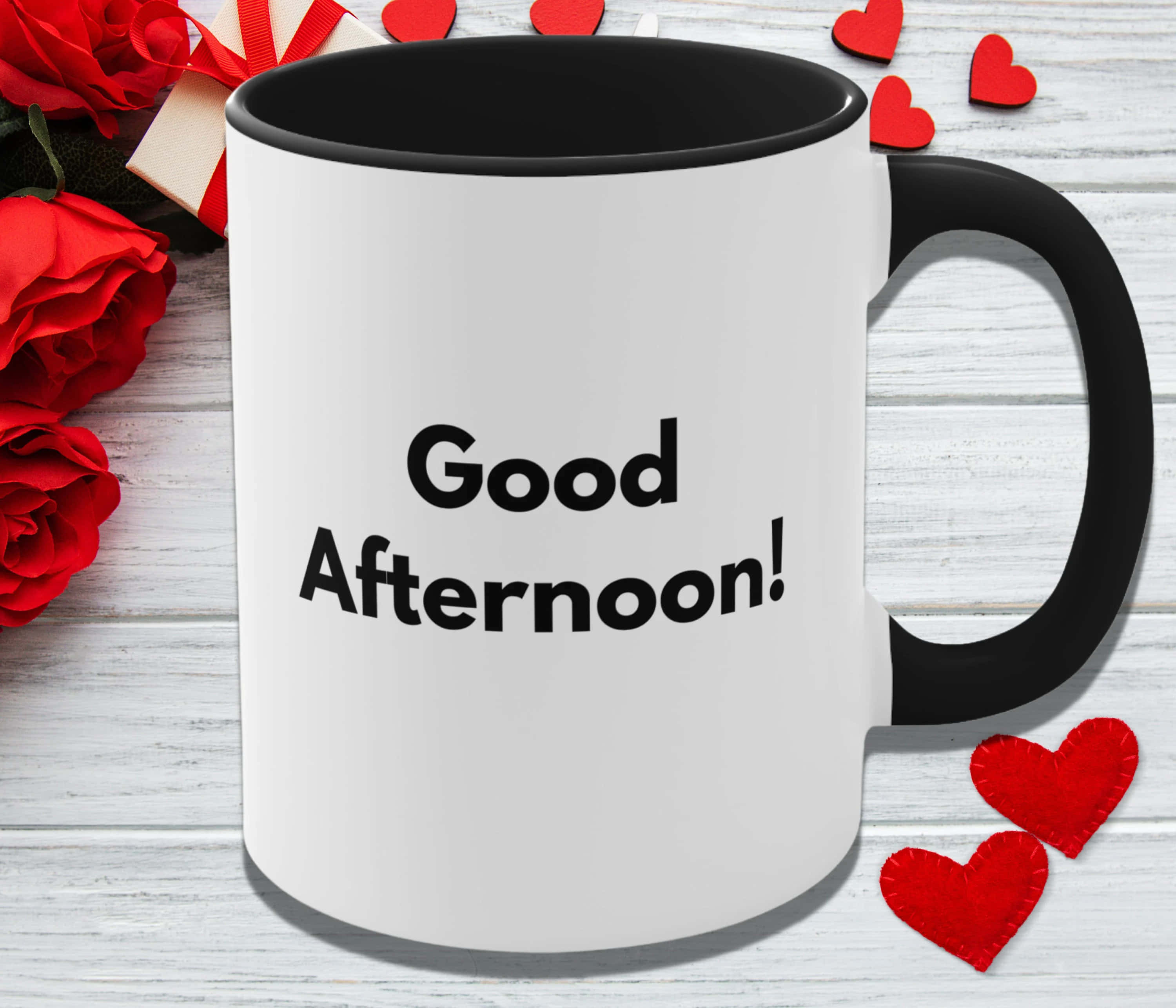 Good Afternoon 桌布 壁紙 — 一個白色馬克杯，帶黑色把手和邊緣，上面寫著 Good Afternoon，周圍環繞著紅玫瑰和氈製心形，放在白色木質表面上。