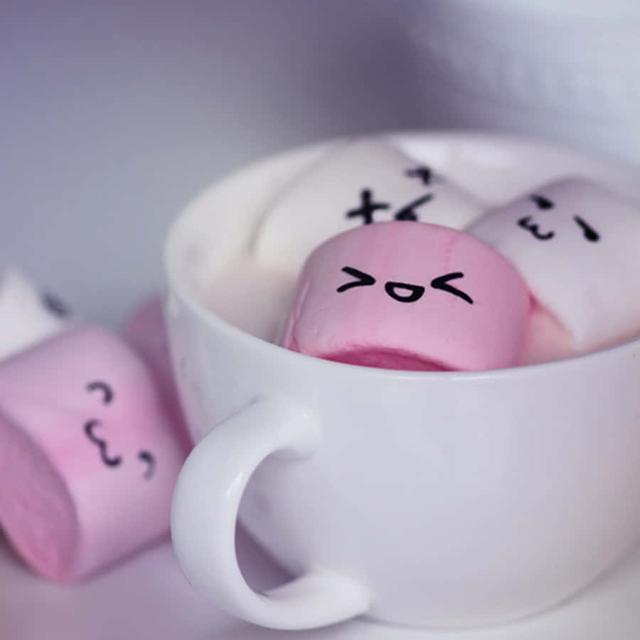 一個白色馬克杯，裝有畫有可愛臉孔的粉紅色和白色棉花糖。 — Squishmallows 壁紙